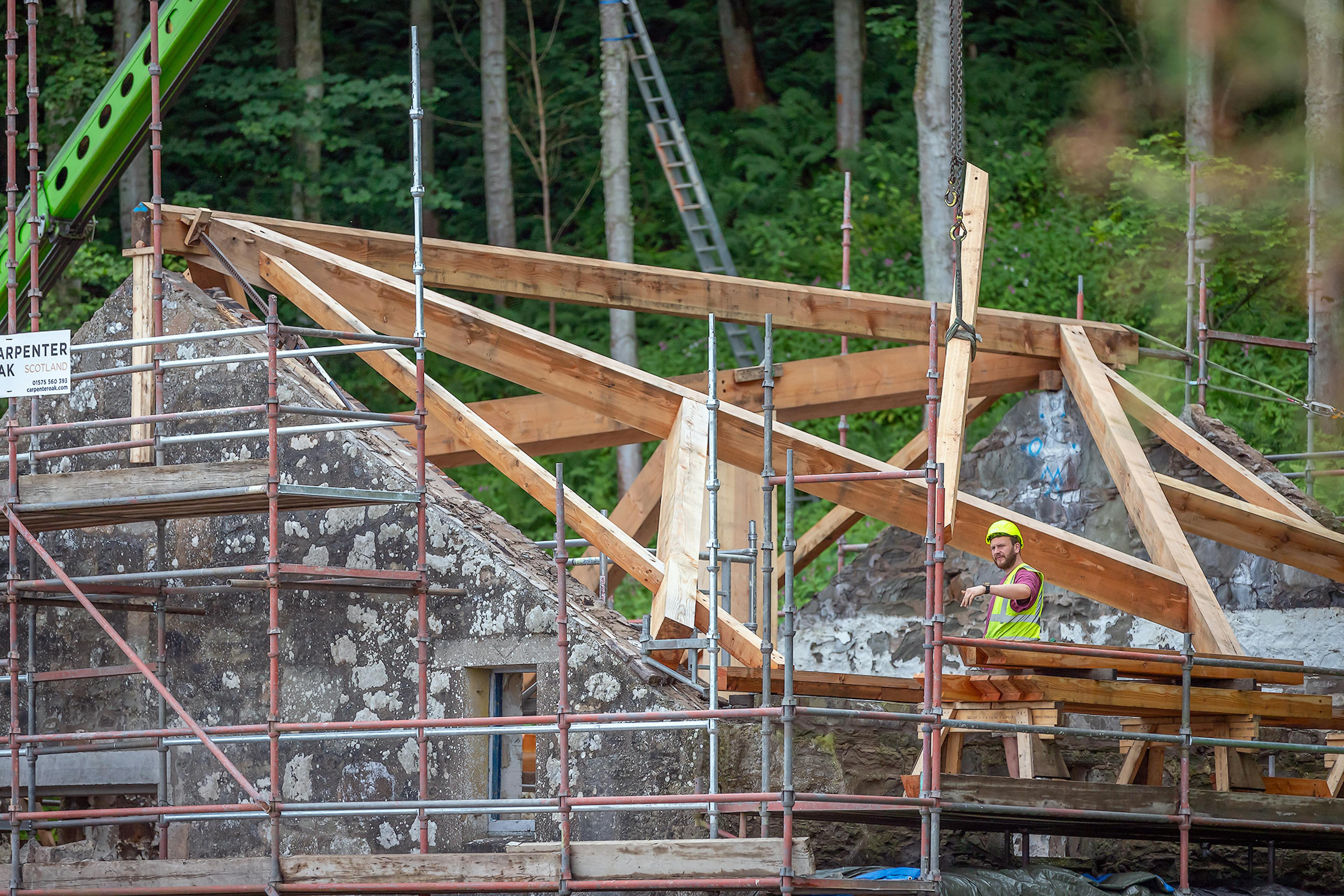 Crane lifting a central post while carpenters guide it into place during the on-site assembly of the Riverside Boathouse, made from Douglas fir and larch.