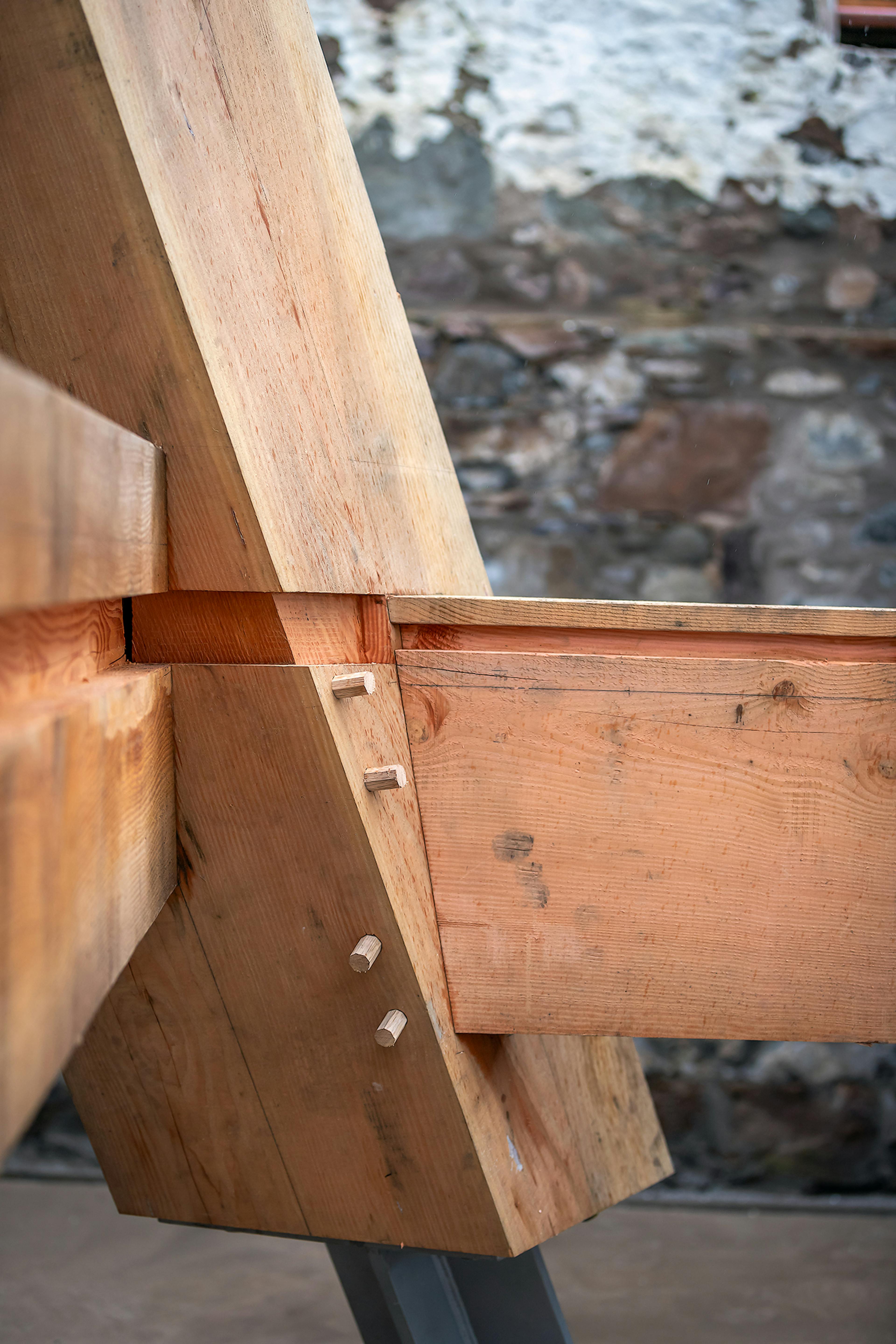Central post of the Riverside Boathouse being installed on site, showing steel post feet and joinery connections with pegs, using Douglas fir and larch timbers