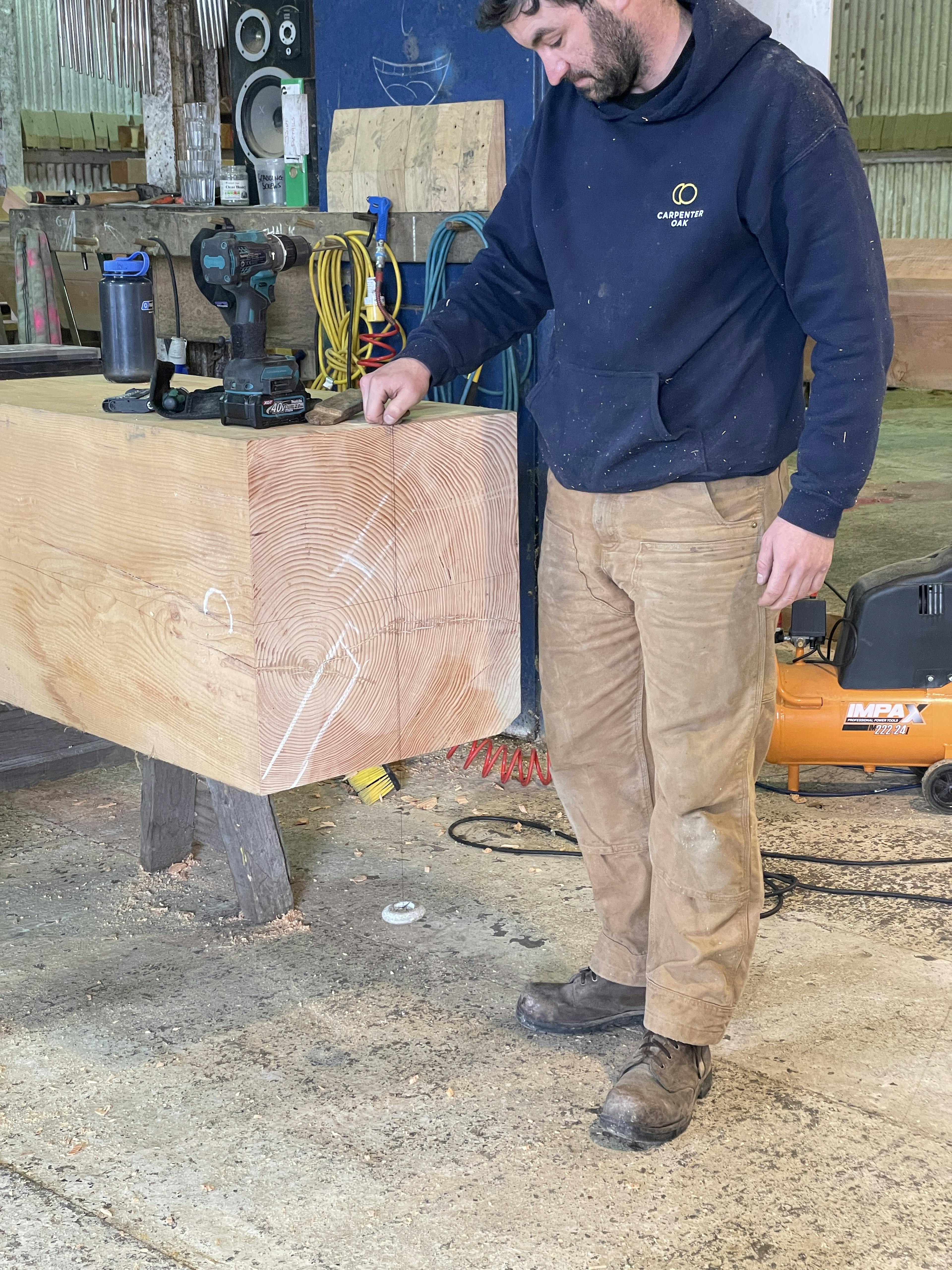 Carpenter working on a full timber post in the workshop for the Riverside Boathouse, using Douglas fir and larch