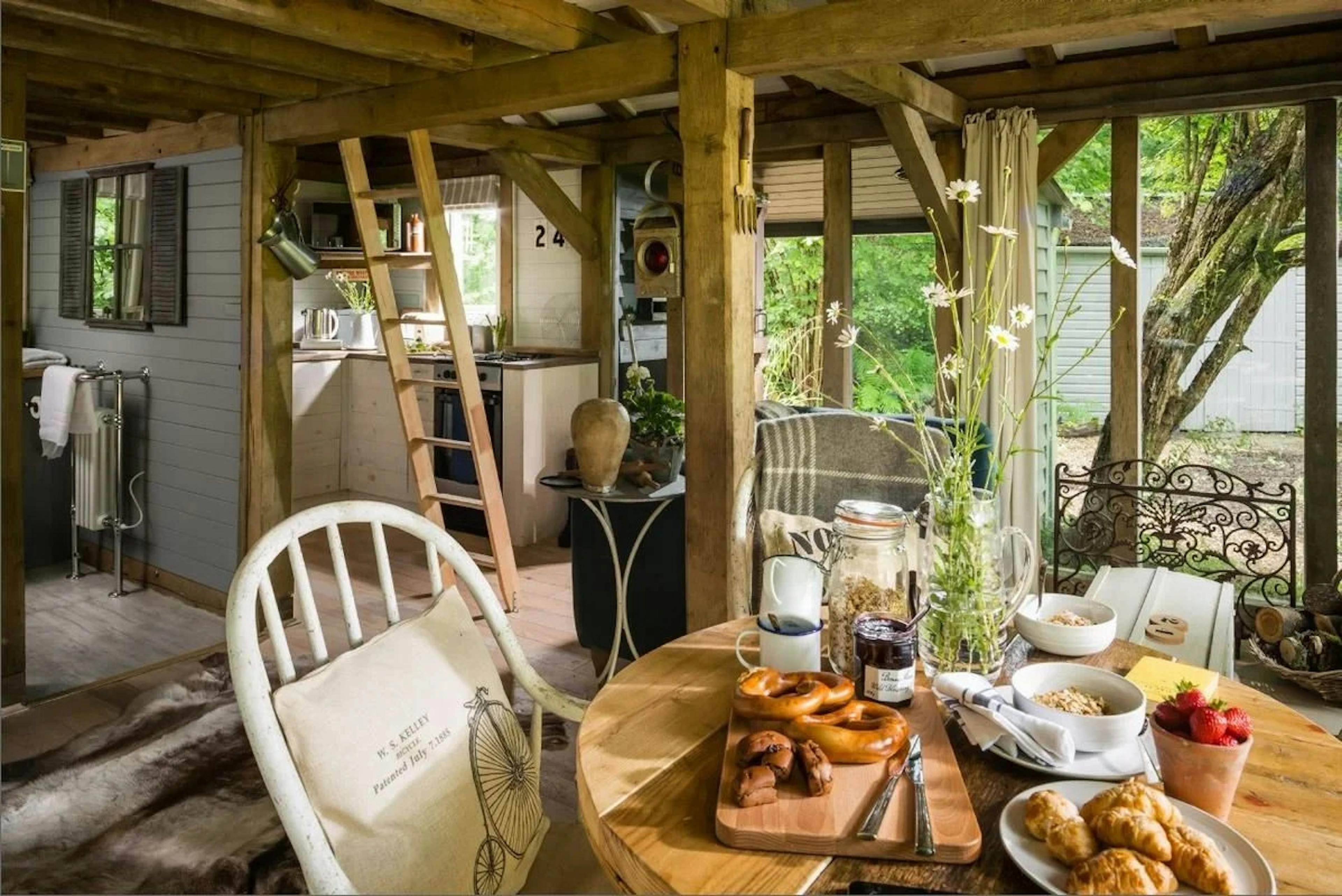 An open plan oak framed cabin with dining and kitchen areas and a ladder to a mezzanine level