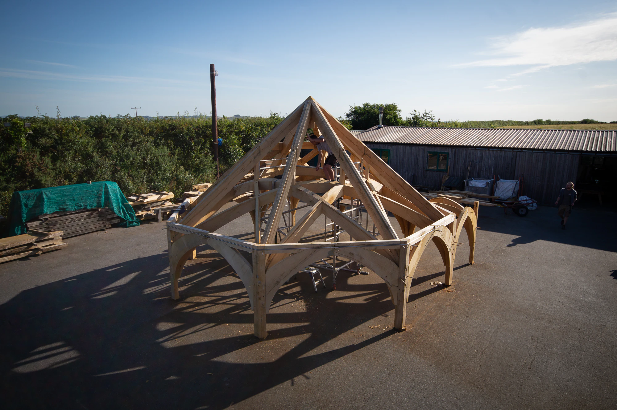 Timber frame for Radley College being assembled in the Carpenter Oak workshop, designed by Purcell Architects, showing workers fitting large wooden beams and joints.