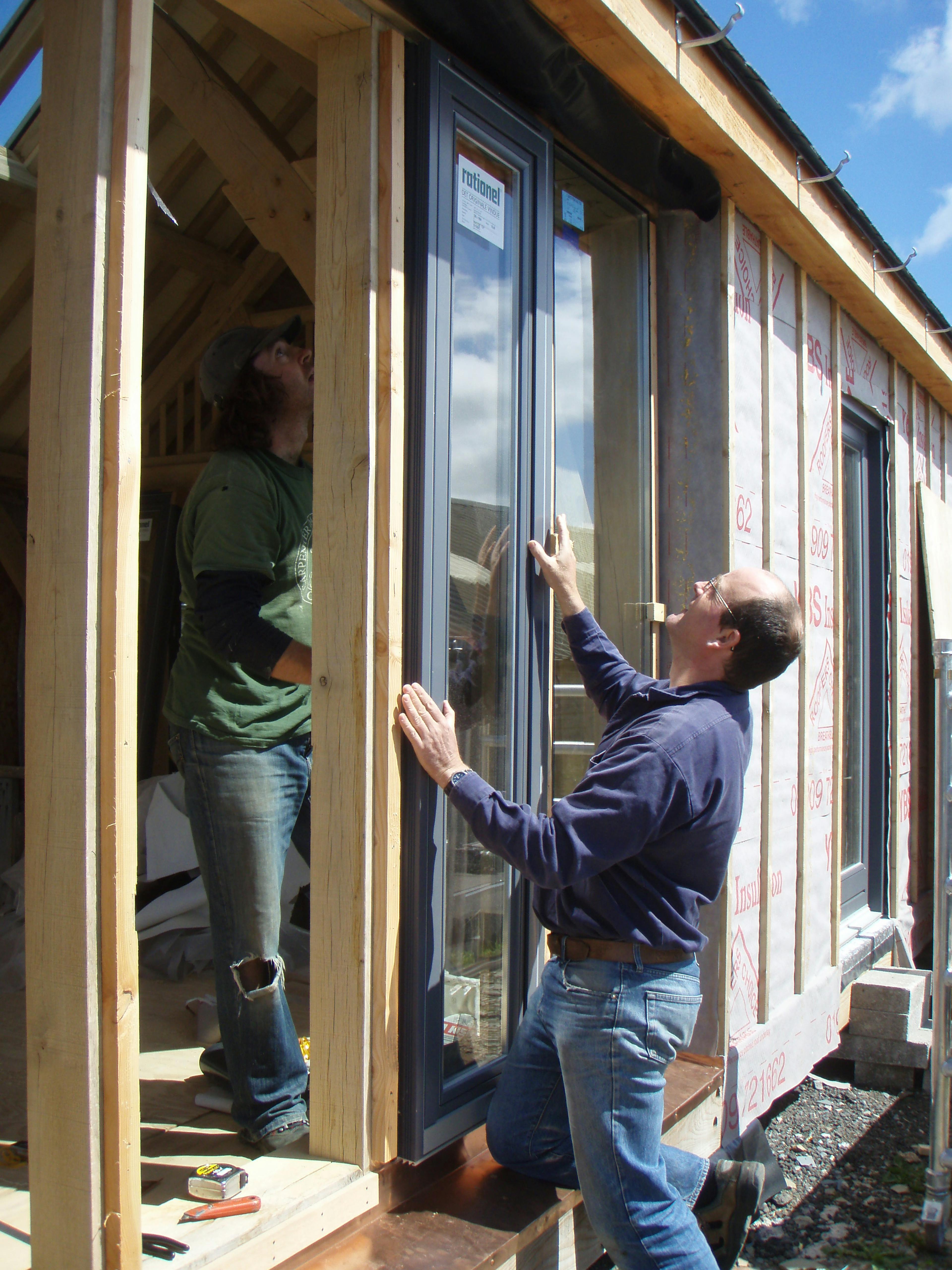 Carpenter Oak team, including Adam, installing large glass panels for direct glazing at the show barn in East Cornworthy, highlighting teamwork, precision, and timber frame construction