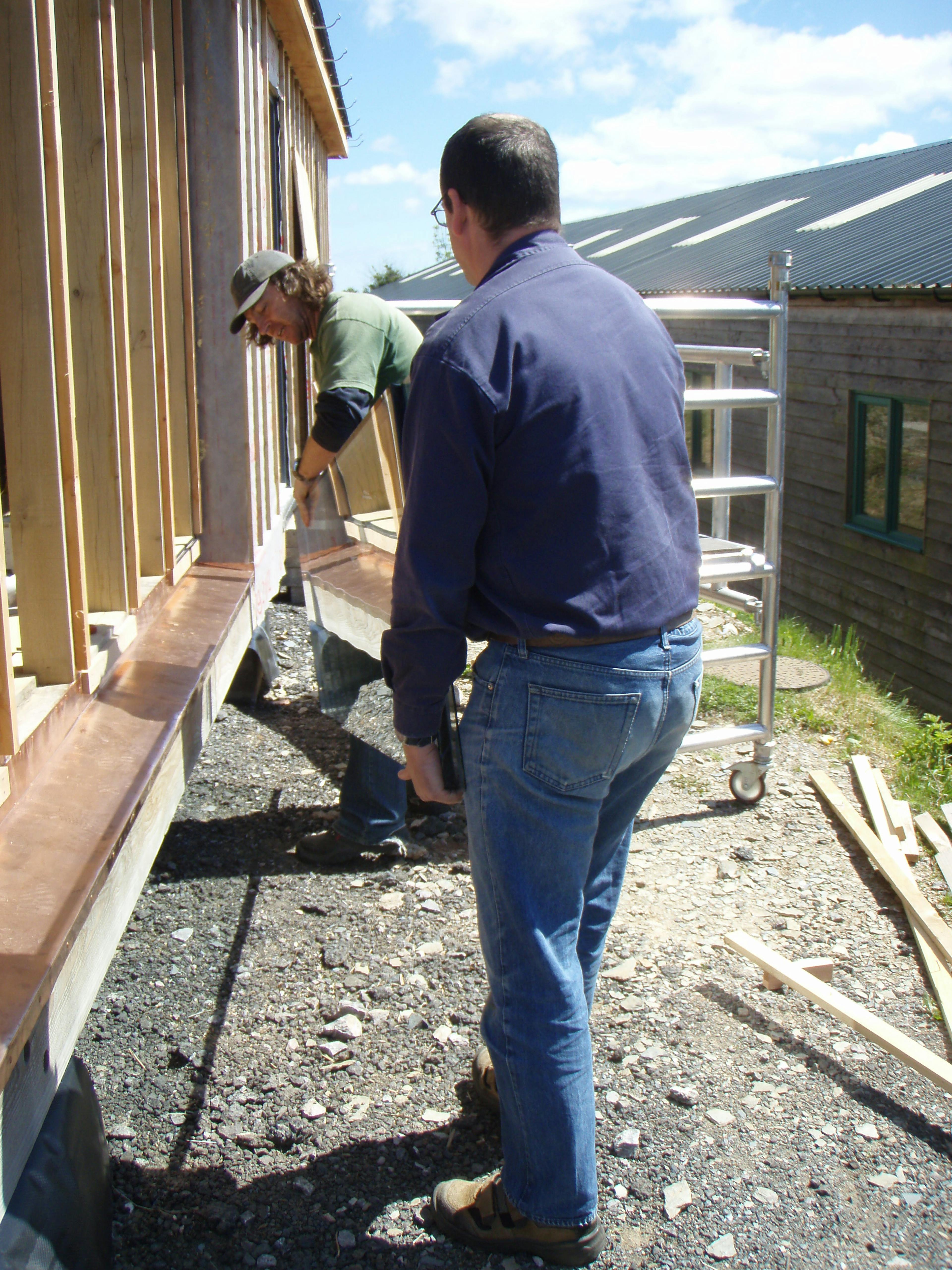 Carpenter Oak team member Adam installing direct glazing at the show barn in East Cornworthy, highlighting teamwork, precision, and timber frame construction