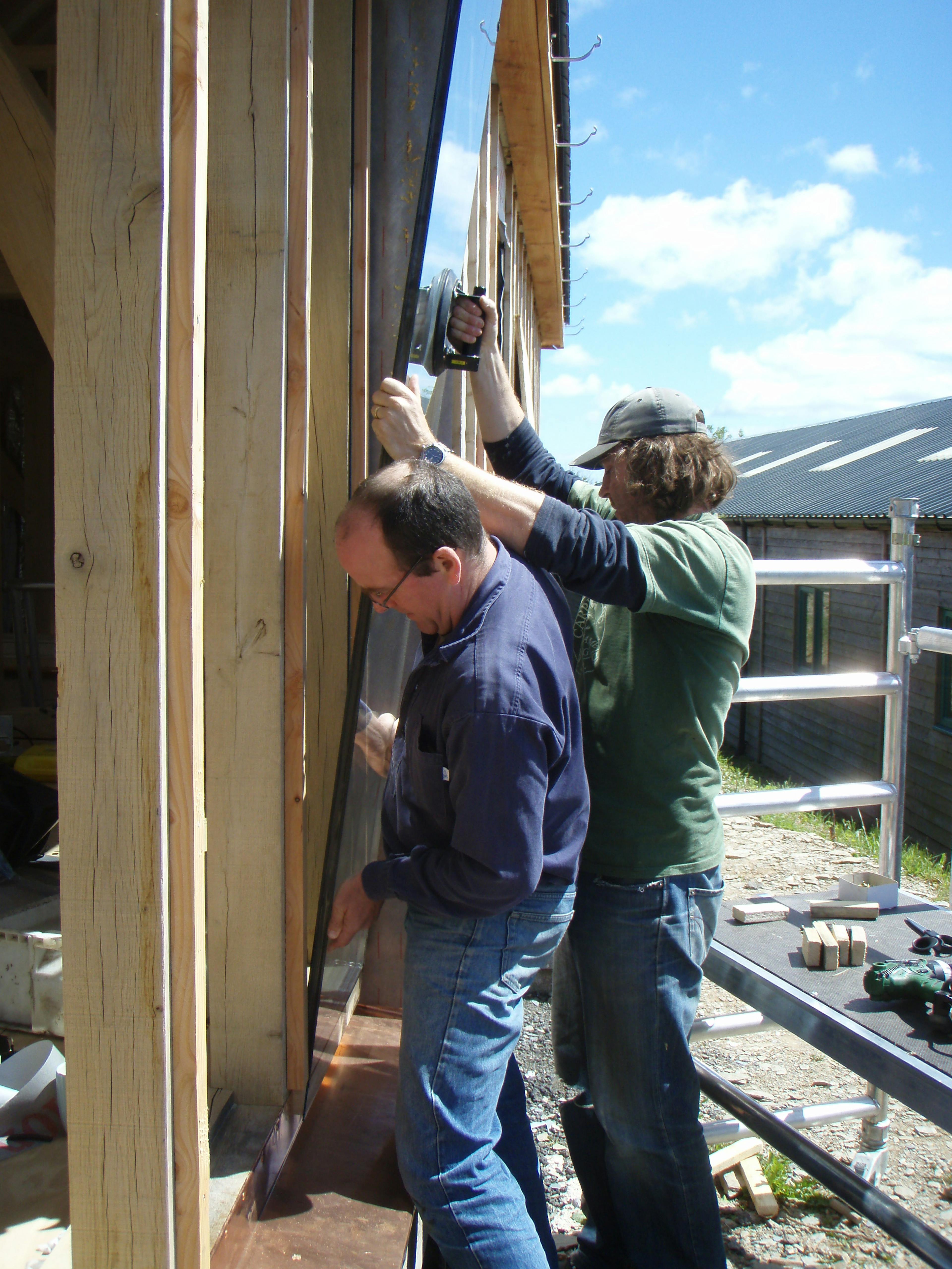 Carpenter Oak team member Adam installing large glass panels for direct glazing at the show barn in East Cornworthy, showcasing precise craftsmanship and timber frame integration.