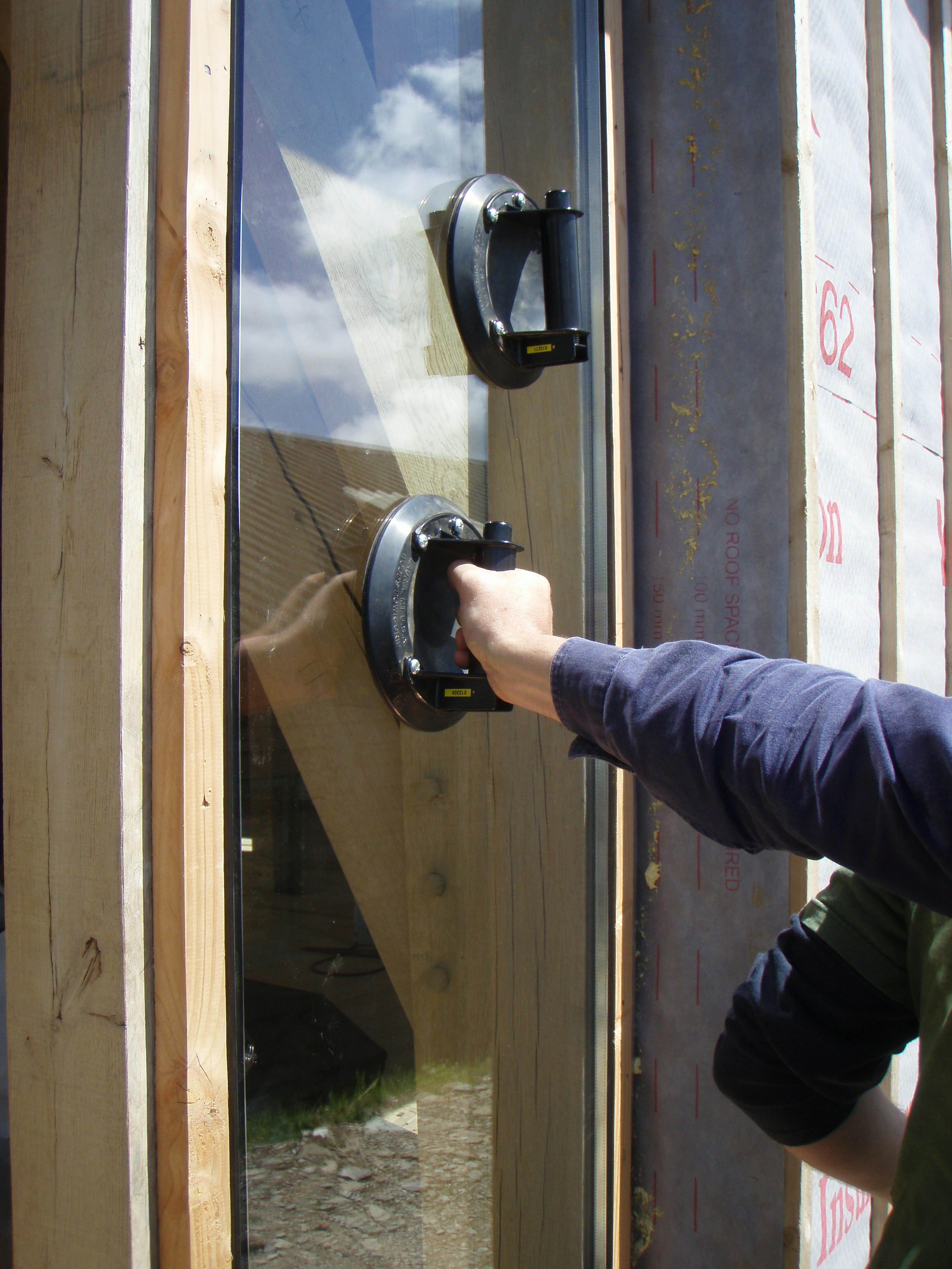 Carpenter Oak team member Adam installing large glass panels with suction cups for direct glazing at the show barn in East Cornworthy, highlighting precision, safety, and timber frame integration