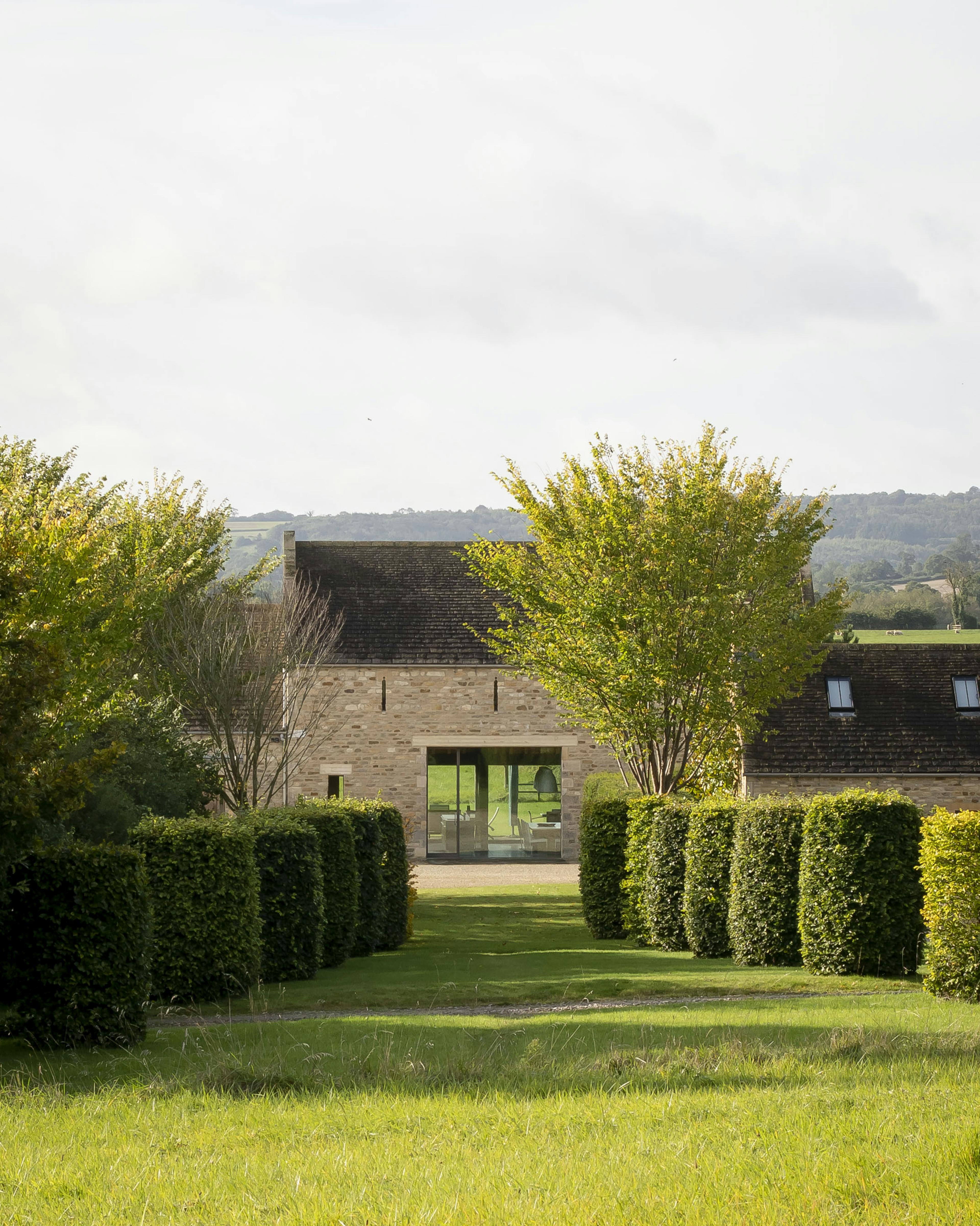 Exterior view of a renovated stone barn featuring an internal oak frame, with an expansive landscaped garden and walkway
