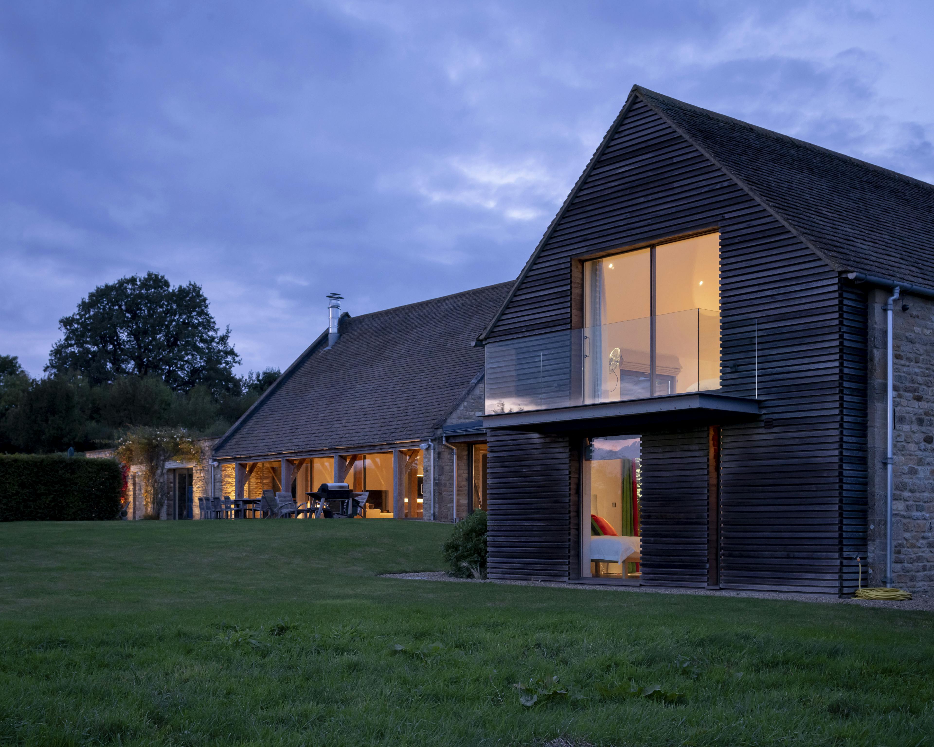 Exterior view of a renovated stone barn with a modern cladded extension, blending rustic charm with contemporary design
