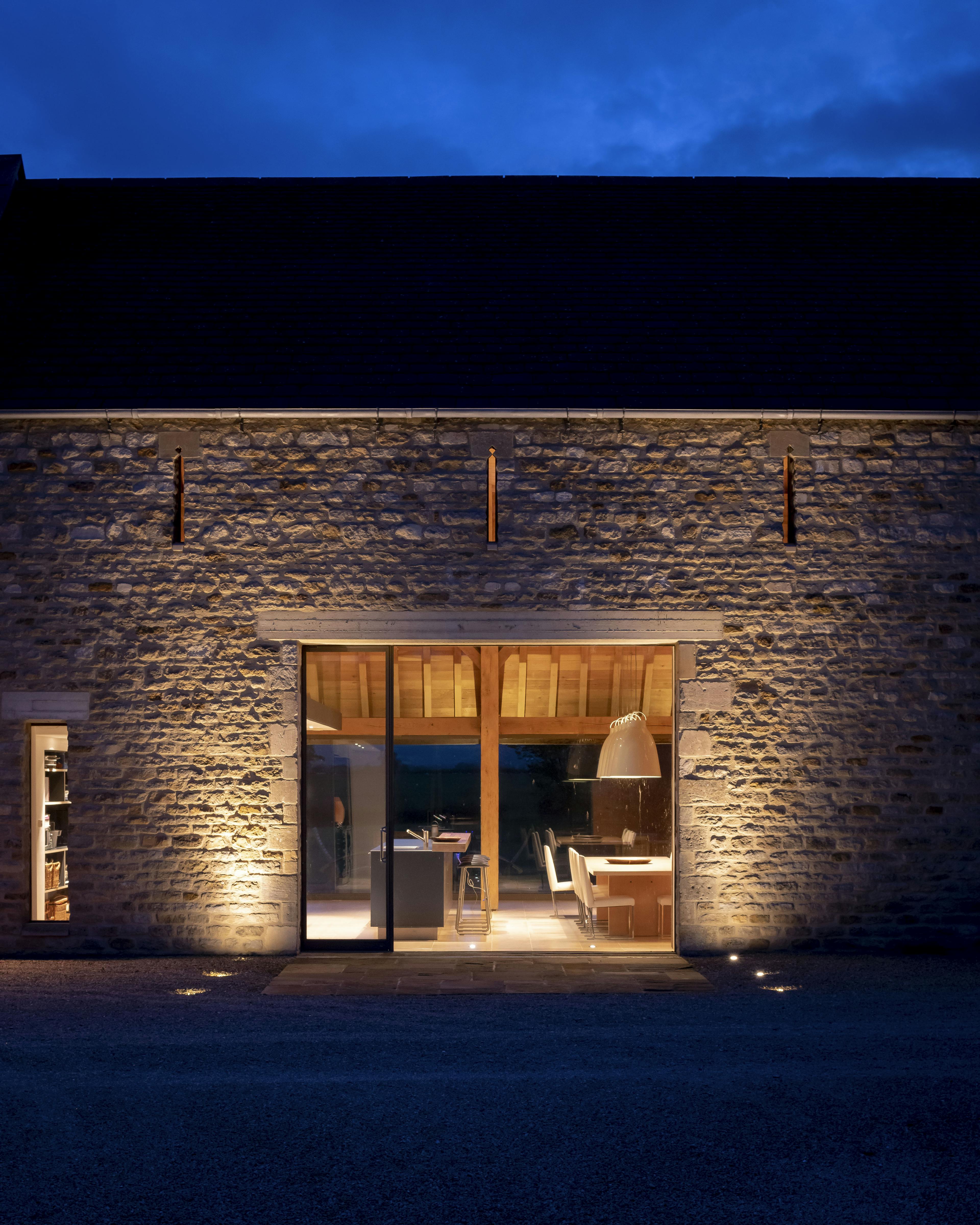 Exterior view of a stone barn undergoing renovation, featuring a visible internal oak frame and a contemporary open-plan living space