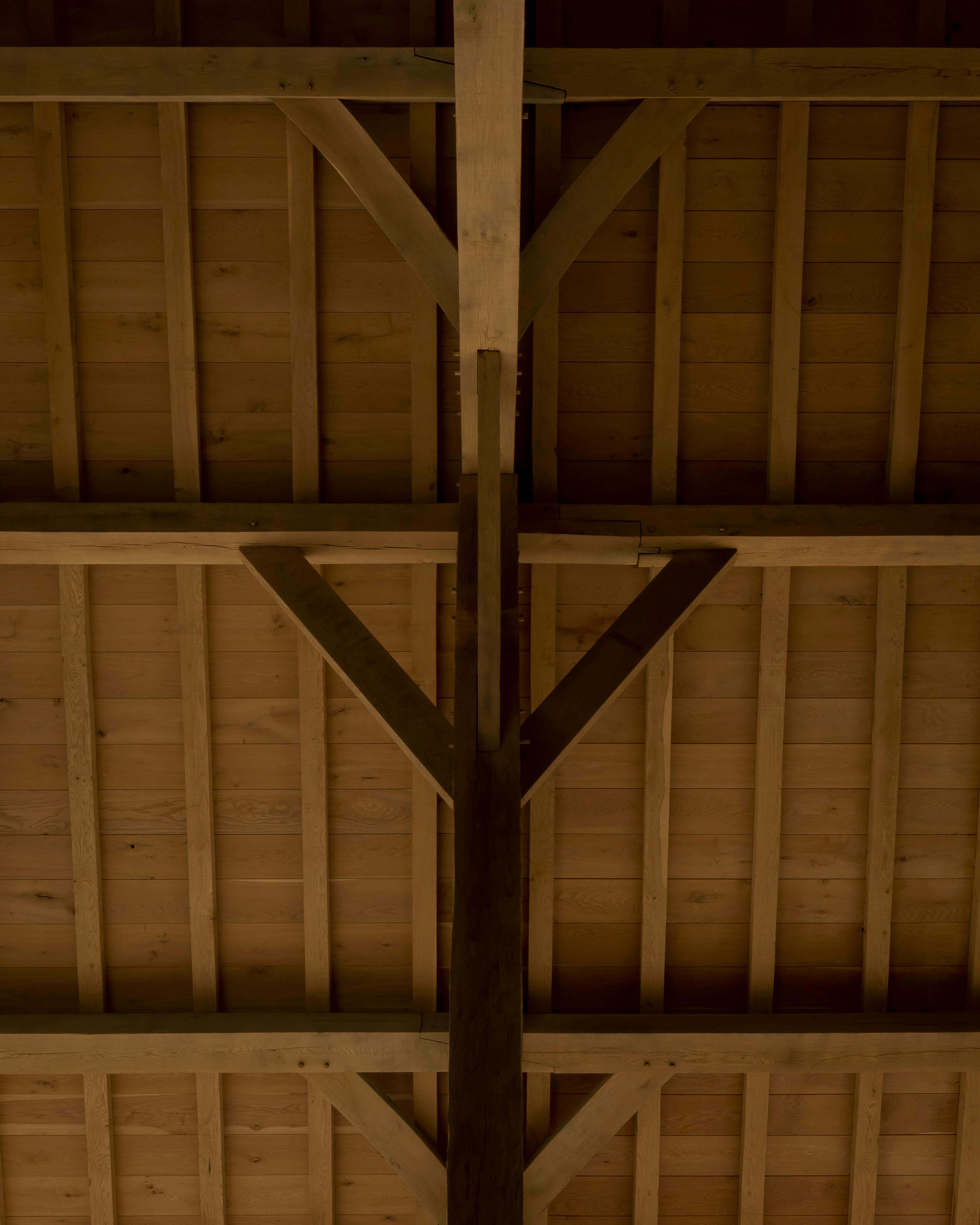 Interior of a renovated oak-framed barn with vaulted ceilings and exposed beams, highlighting detailed timber boarding and traditional wall braces