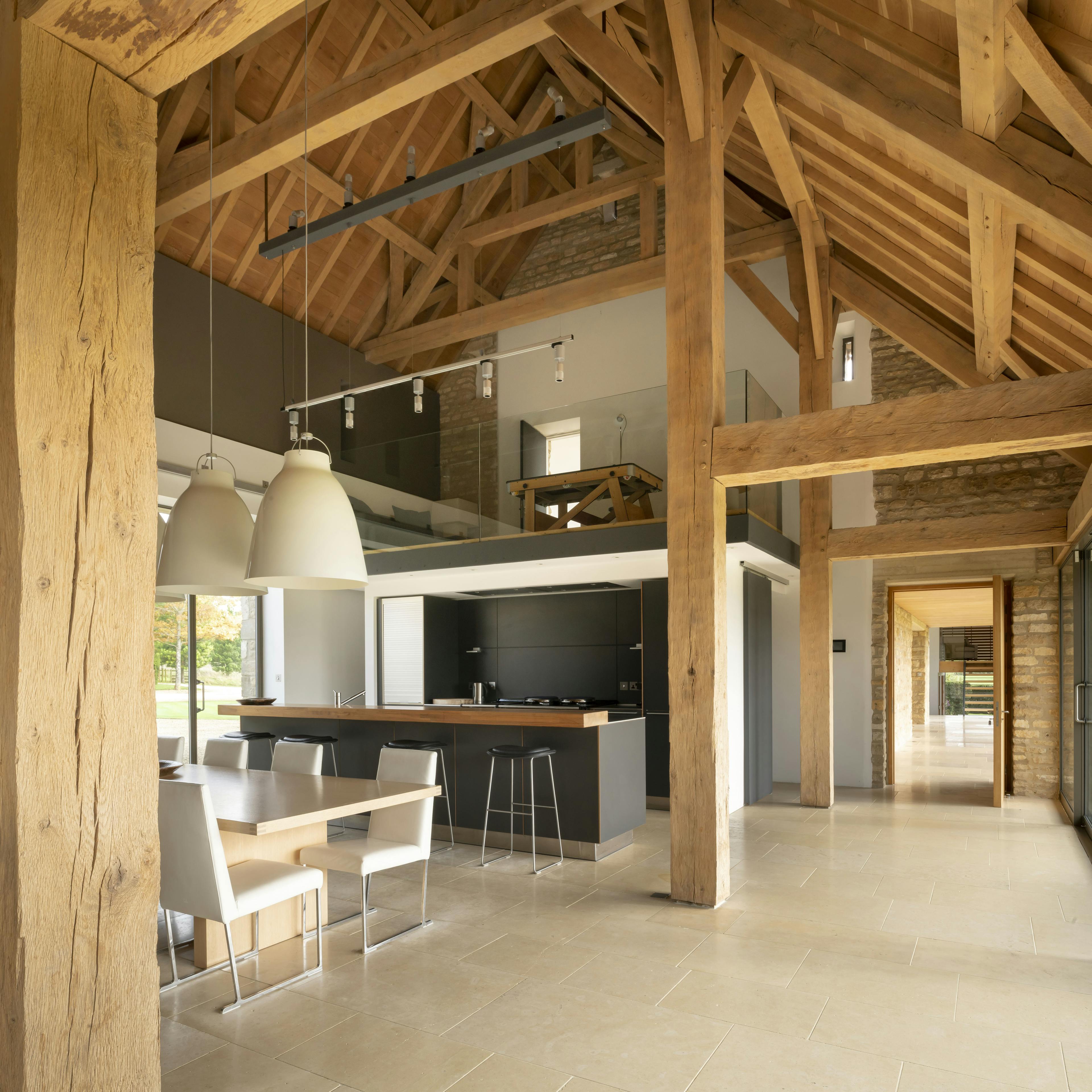 Interior of a spacious renovated oak-framed barn featuring a vaulted ceiling, exposed rustic beams, and a contemporary open-plan living space