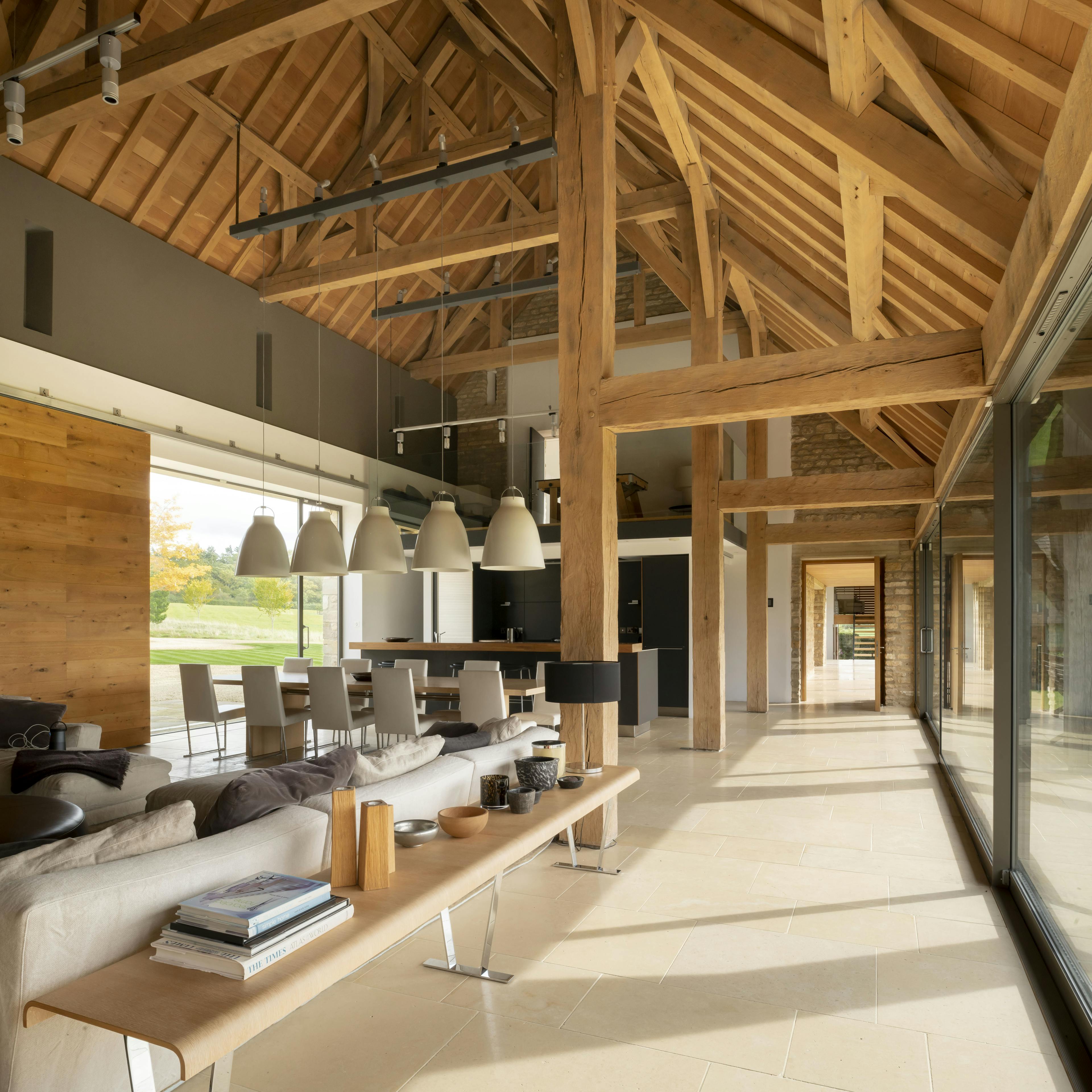 Interior of a spacious renovated oak-framed barn featuring a vaulted ceiling, exposed rustic beams, and a contemporary open-plan kitchen and dining area