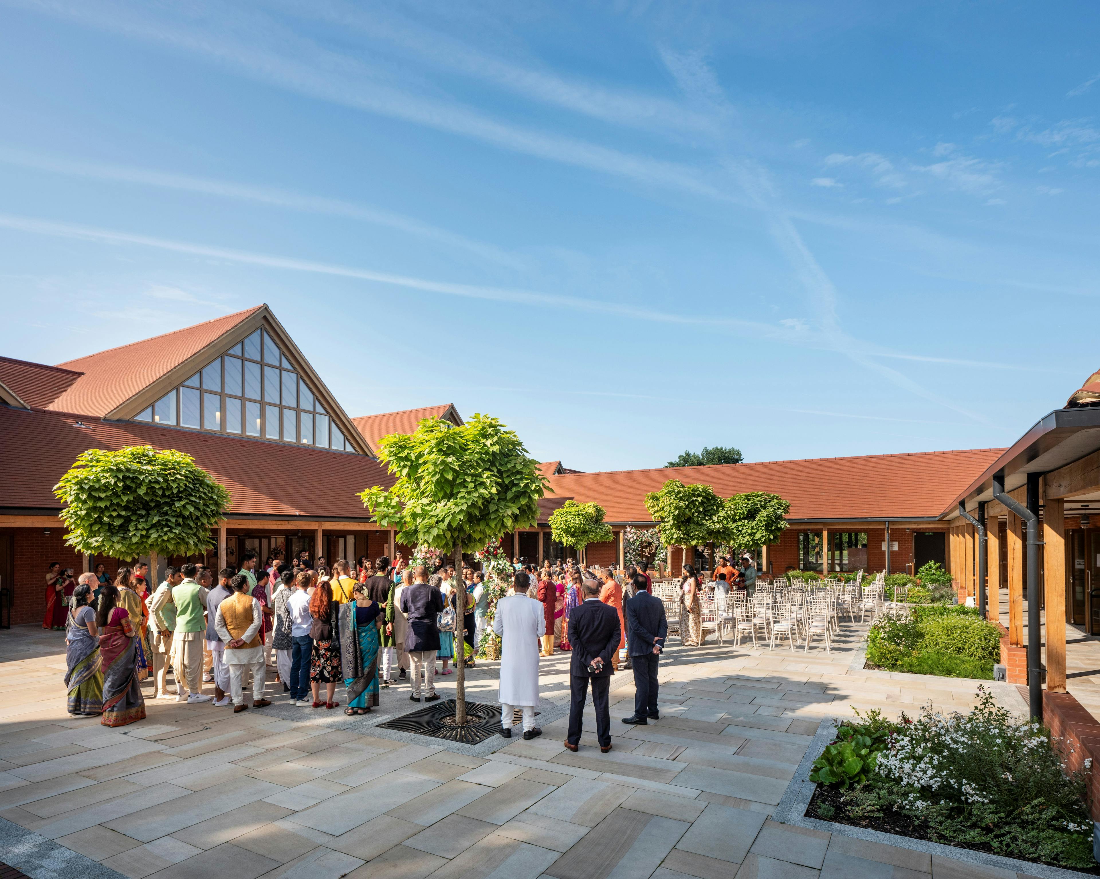 A gathering of people inside a courtyard of a Hindu Temple with green oak framed veranda