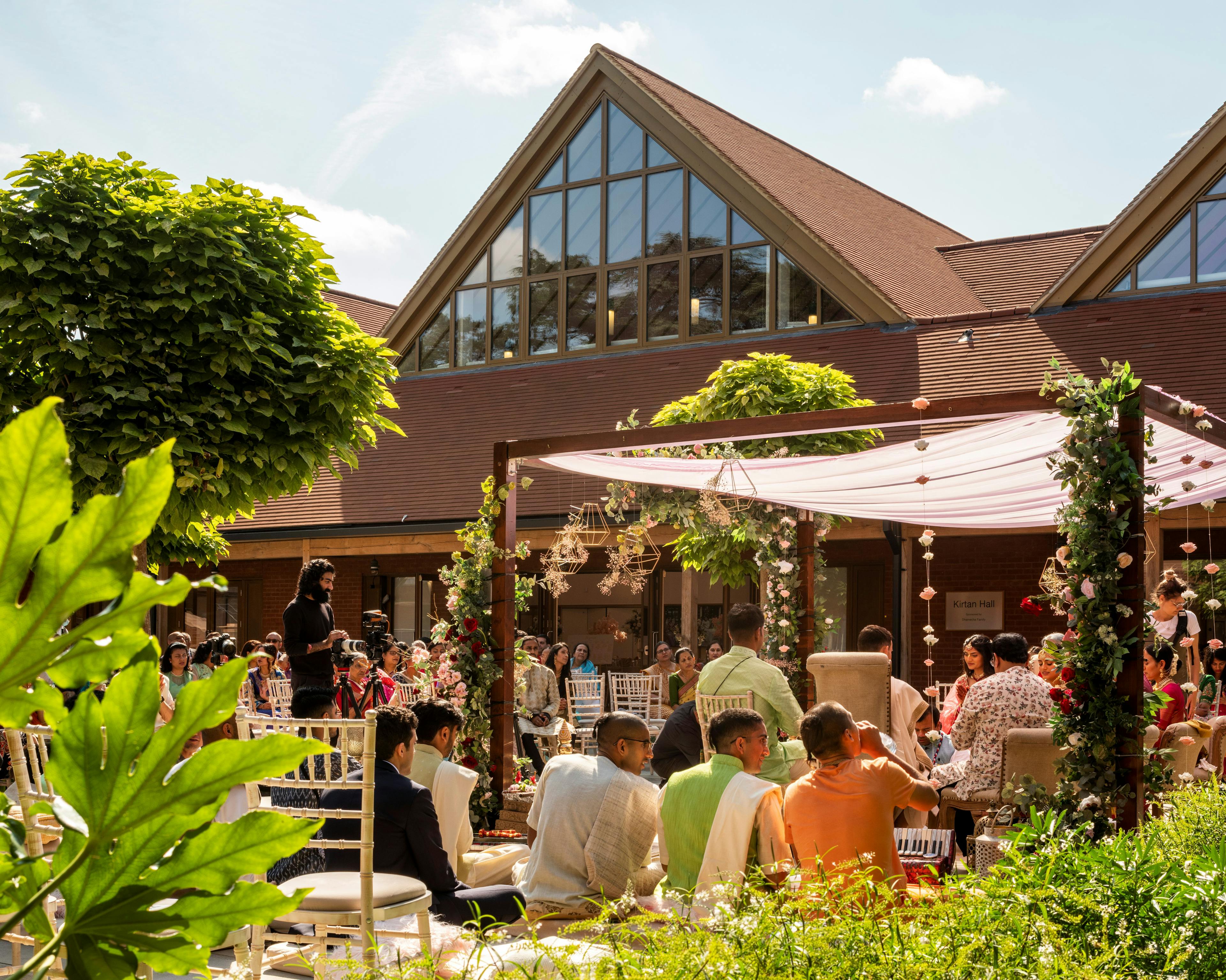 A gathering of people inside a courtyard of a Hindu Temple with green oak framed veranda