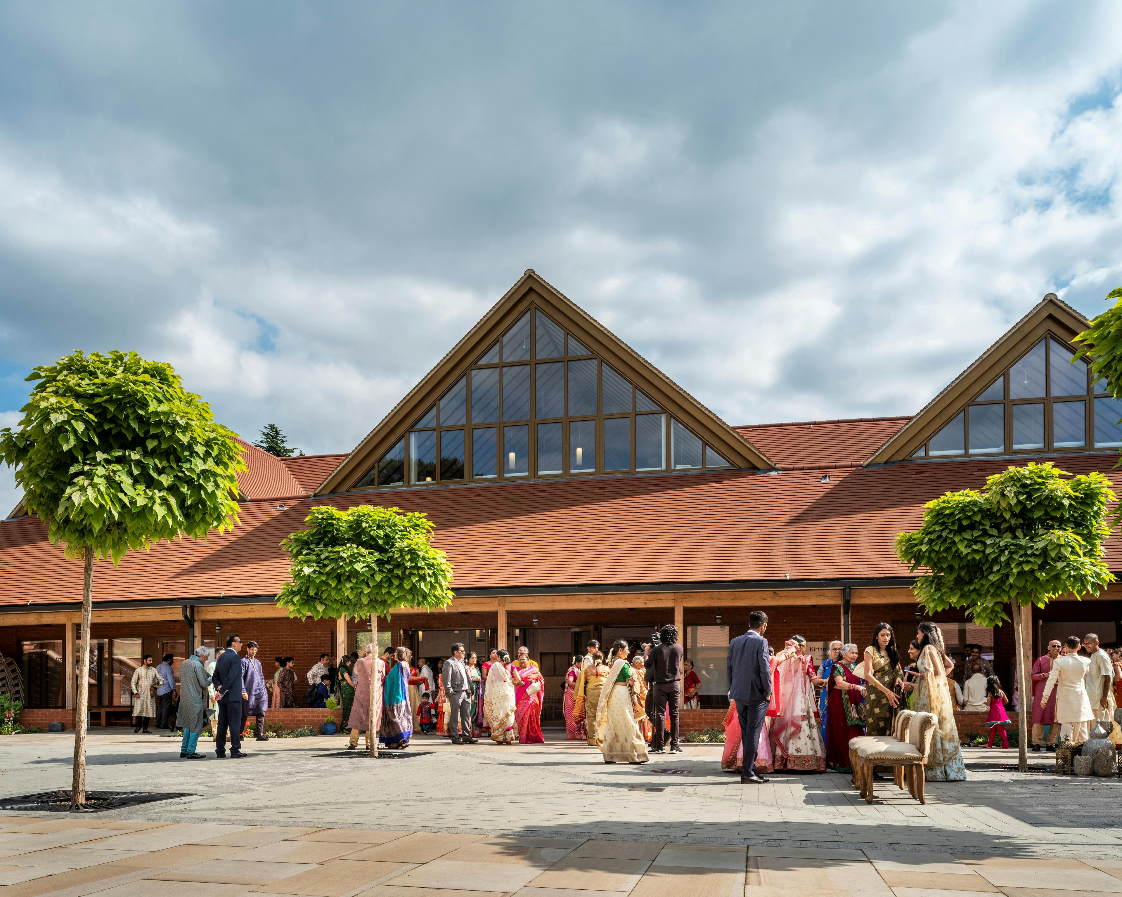 A gathering of people inside a courtyard of a Hindu Temple with green oak framed veranda