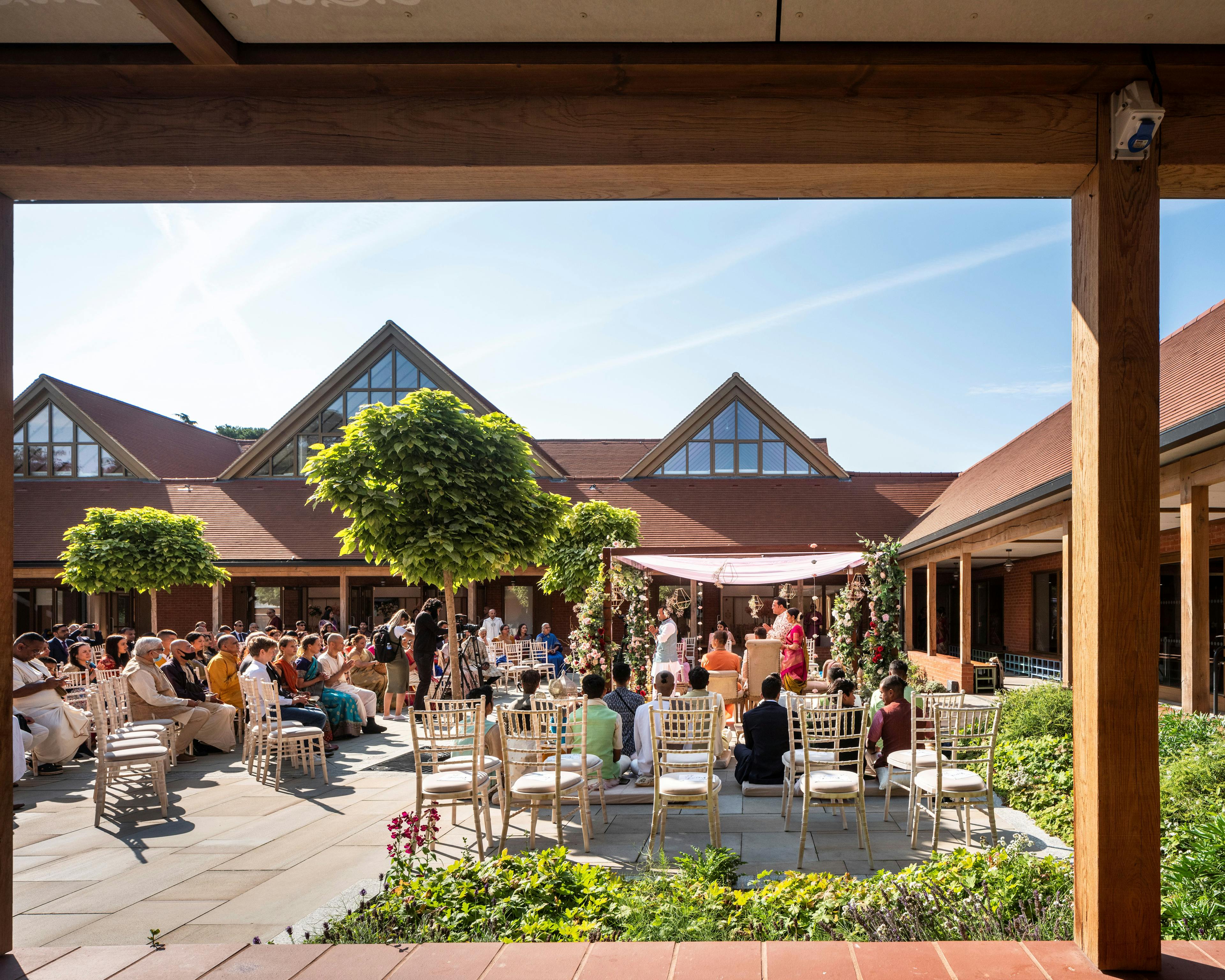 A gathering of people inside a courtyard of a Hindu Temple with green oak framed veranda