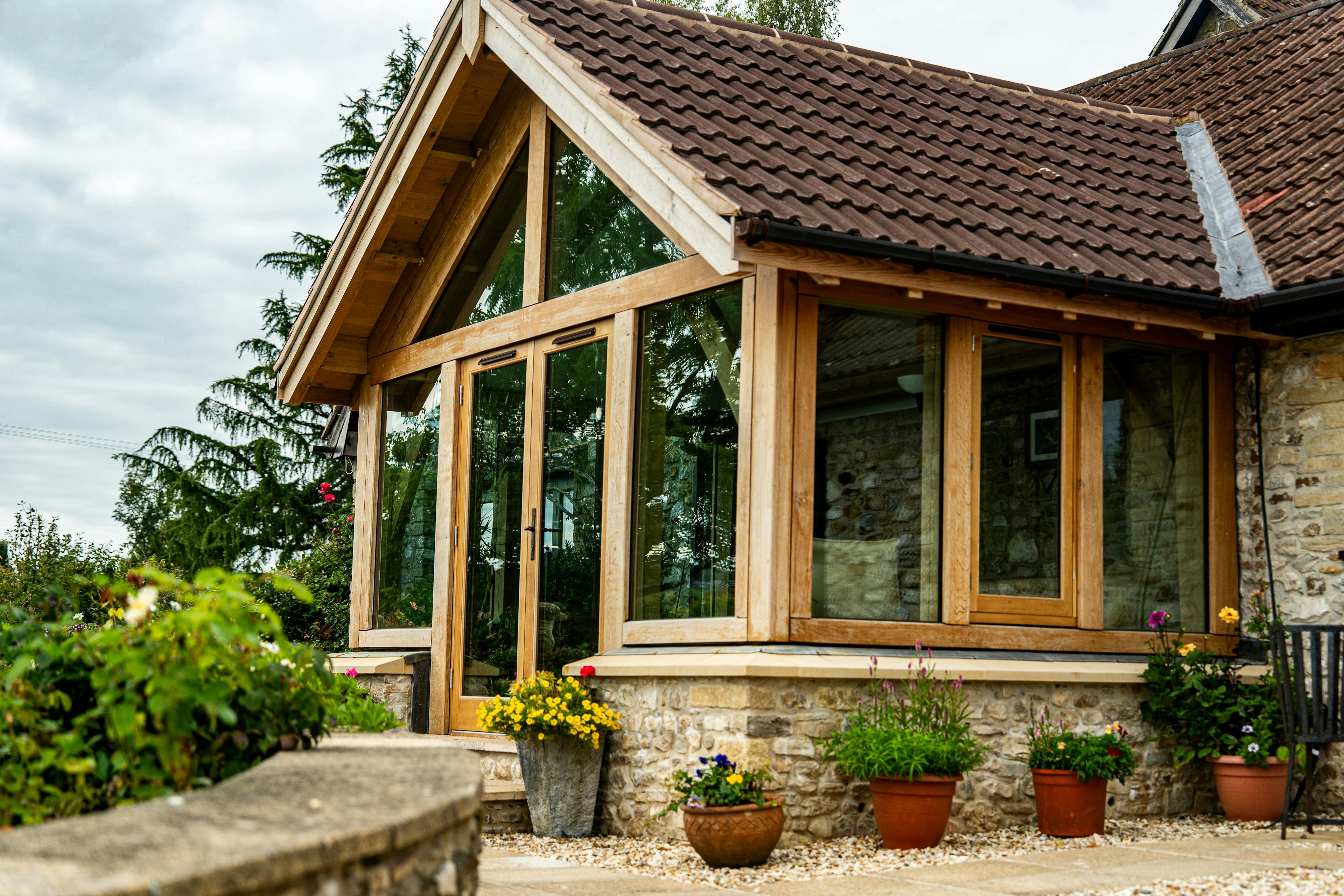Exterior image of an oak frame garden room extension to a home with natural stone cladding, with direct glazing