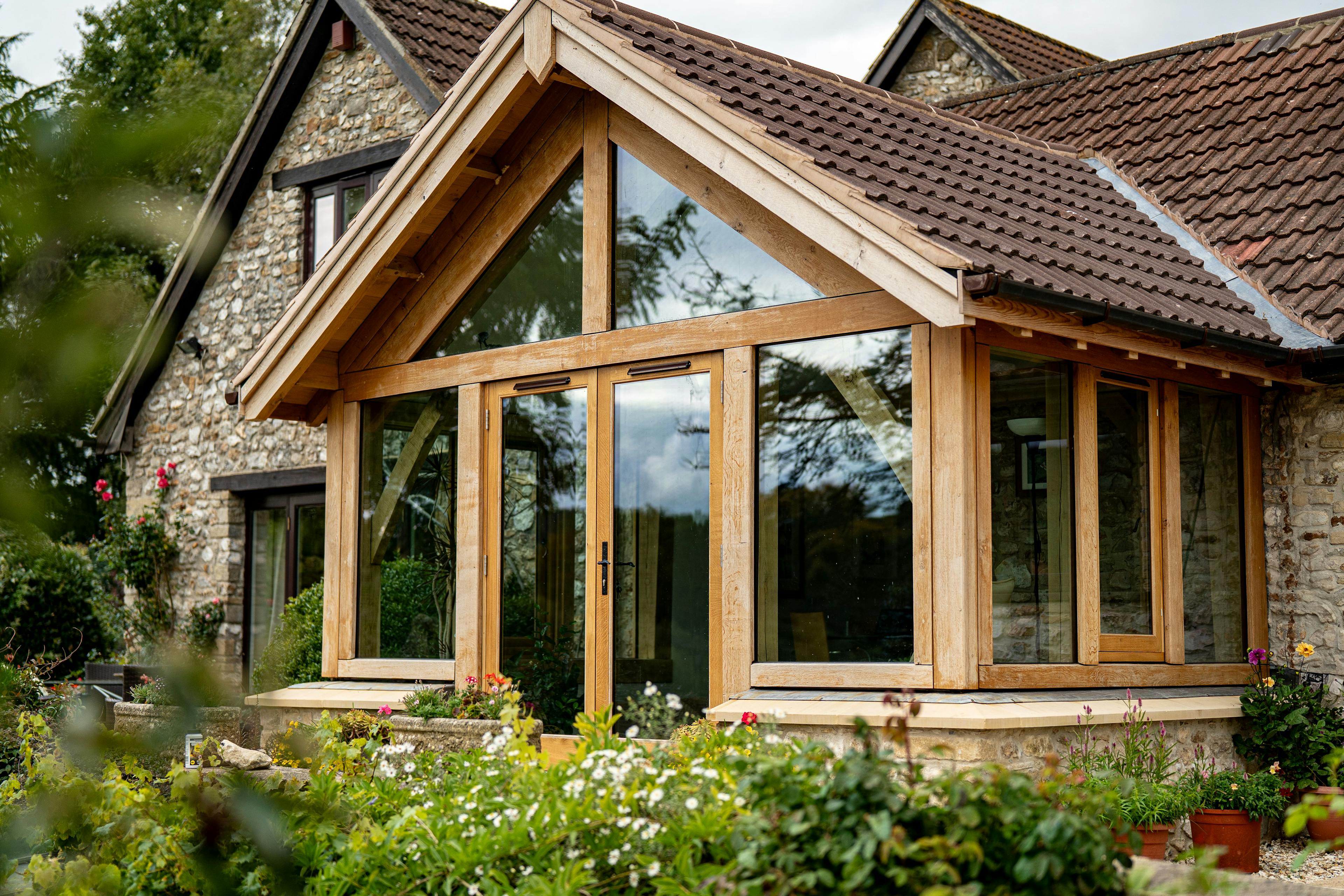 Exterior image of an oak frame garden room extension to a home with natural stone cladding, with direct glazing