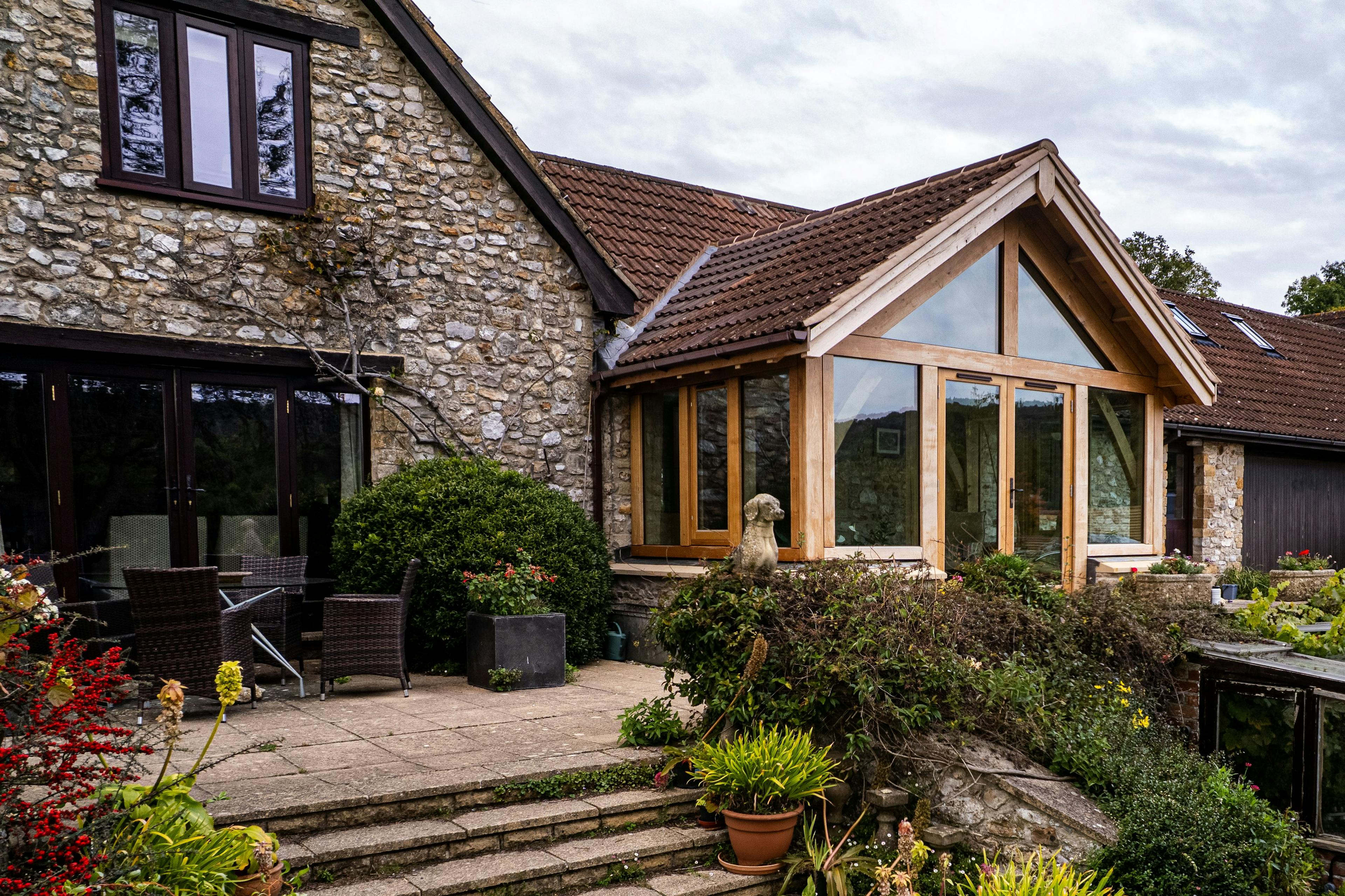 Exterior image of an oak frame garden room extension to a home with natural stone cladding, with direct glazing