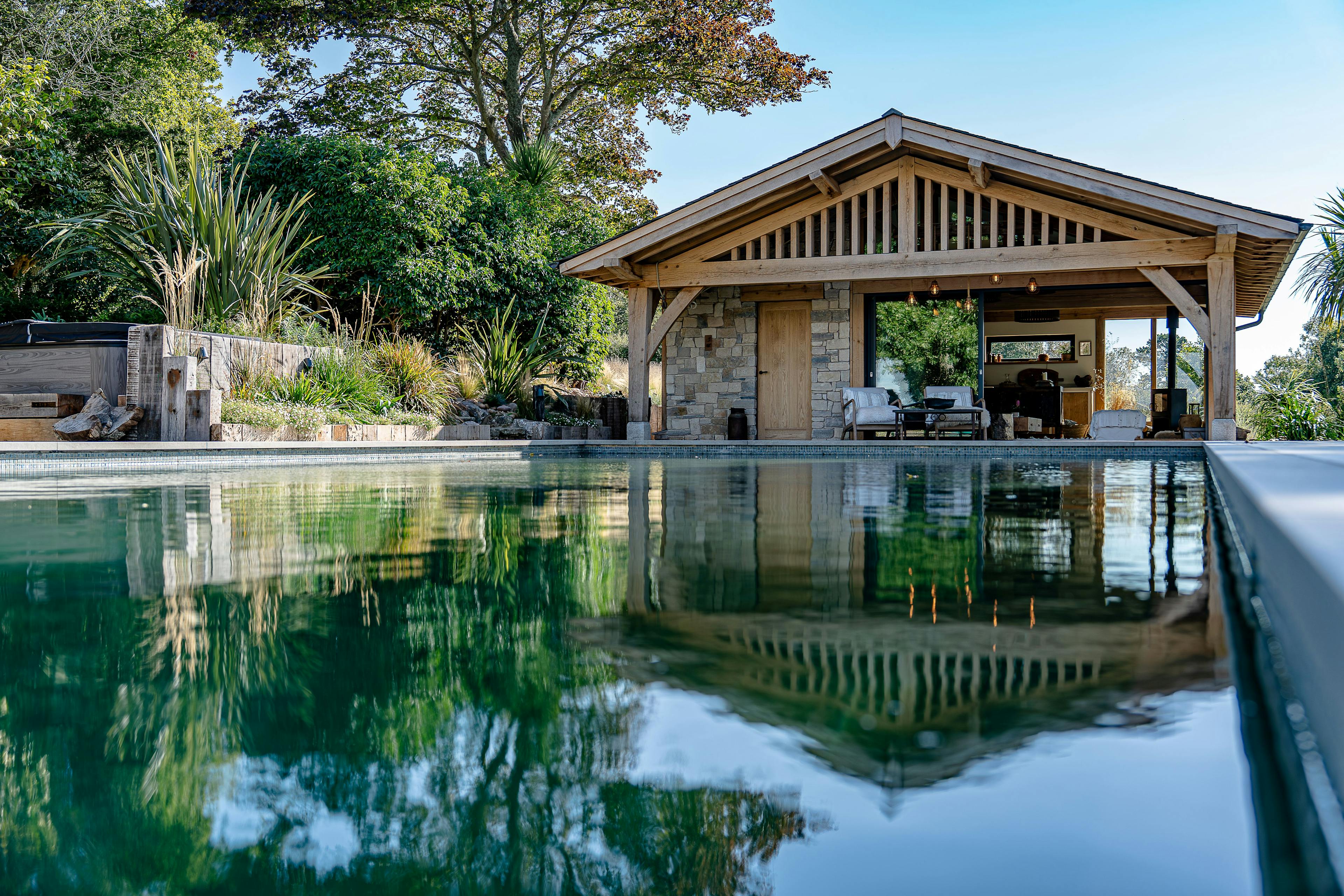 A swimming pool with an oak framed pool building annexe with a low pitch roof and brise soleil