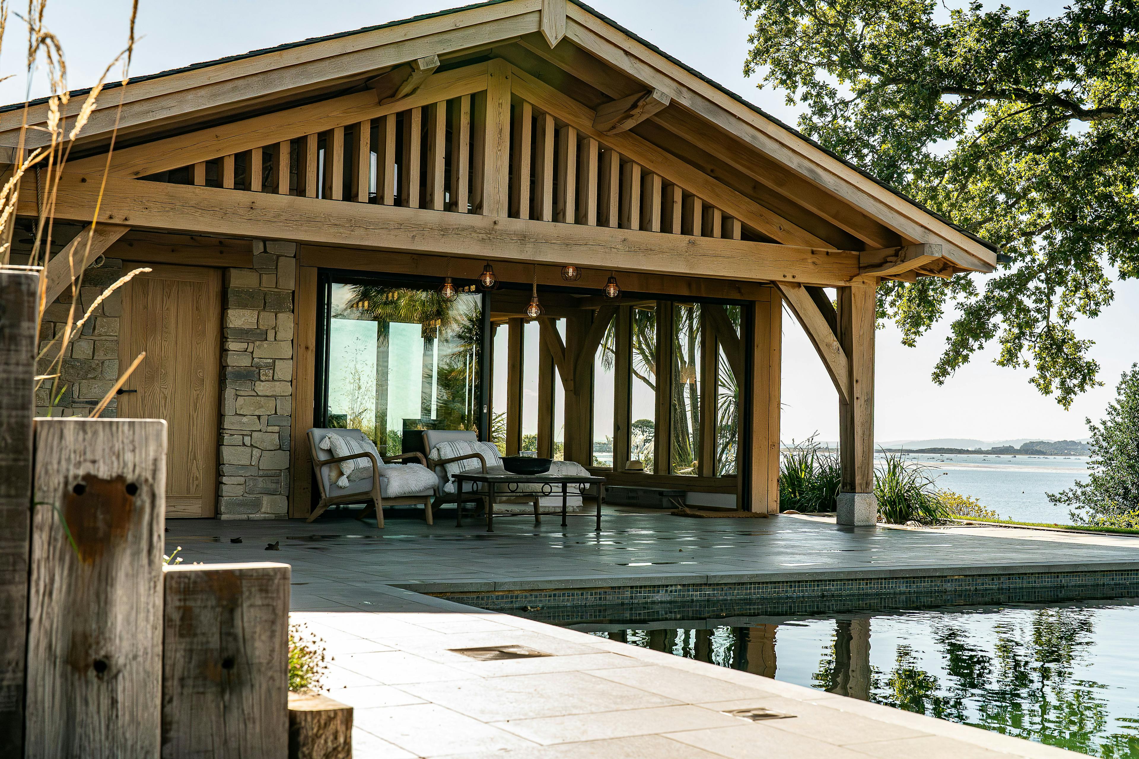 A pool building annexe with an oak frame in a large garden, the sun shines on a swimming pool
