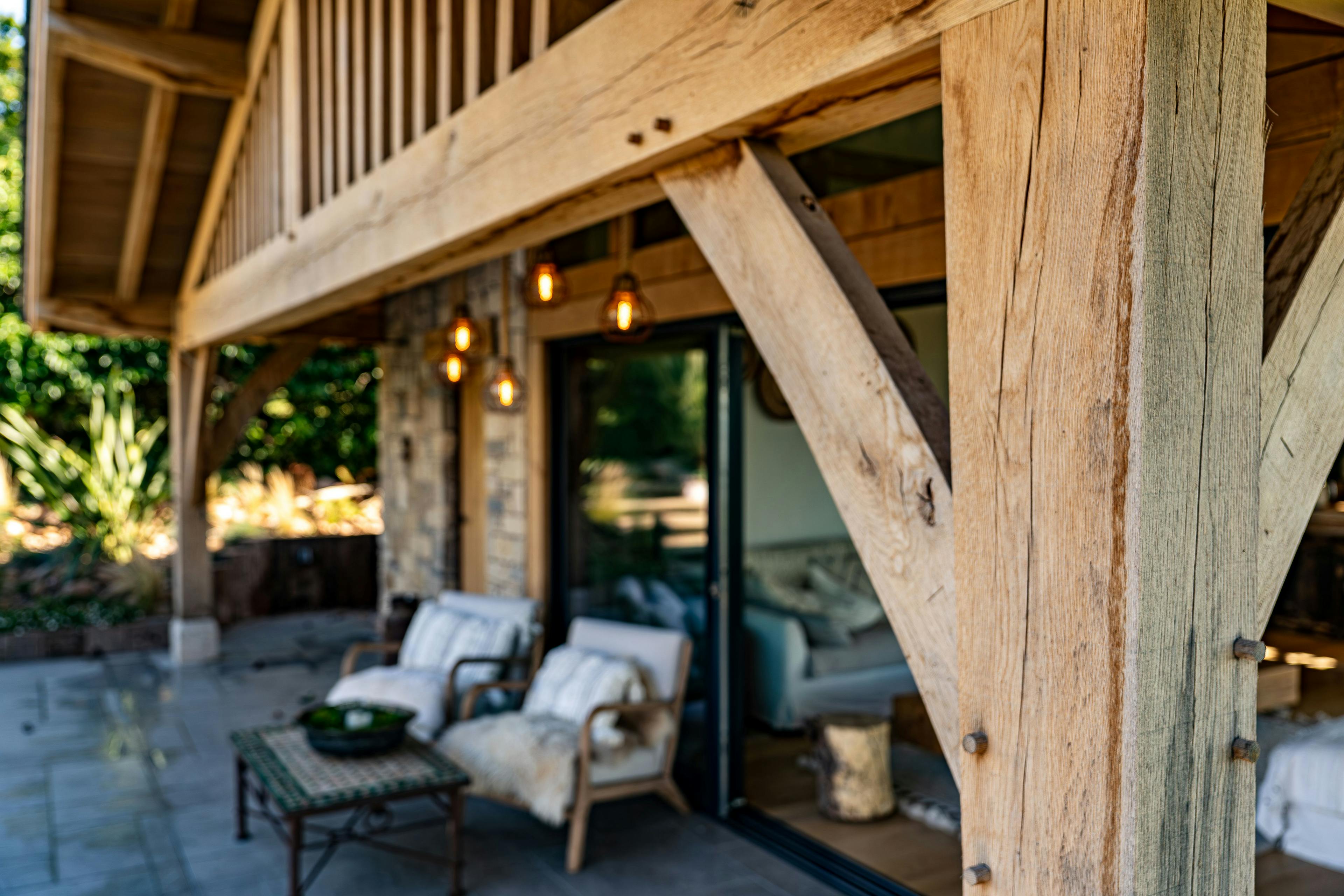 Outdoor seating and patio under the veranda of an oak framed pool building annexe with a low pitch roof and brise soleil