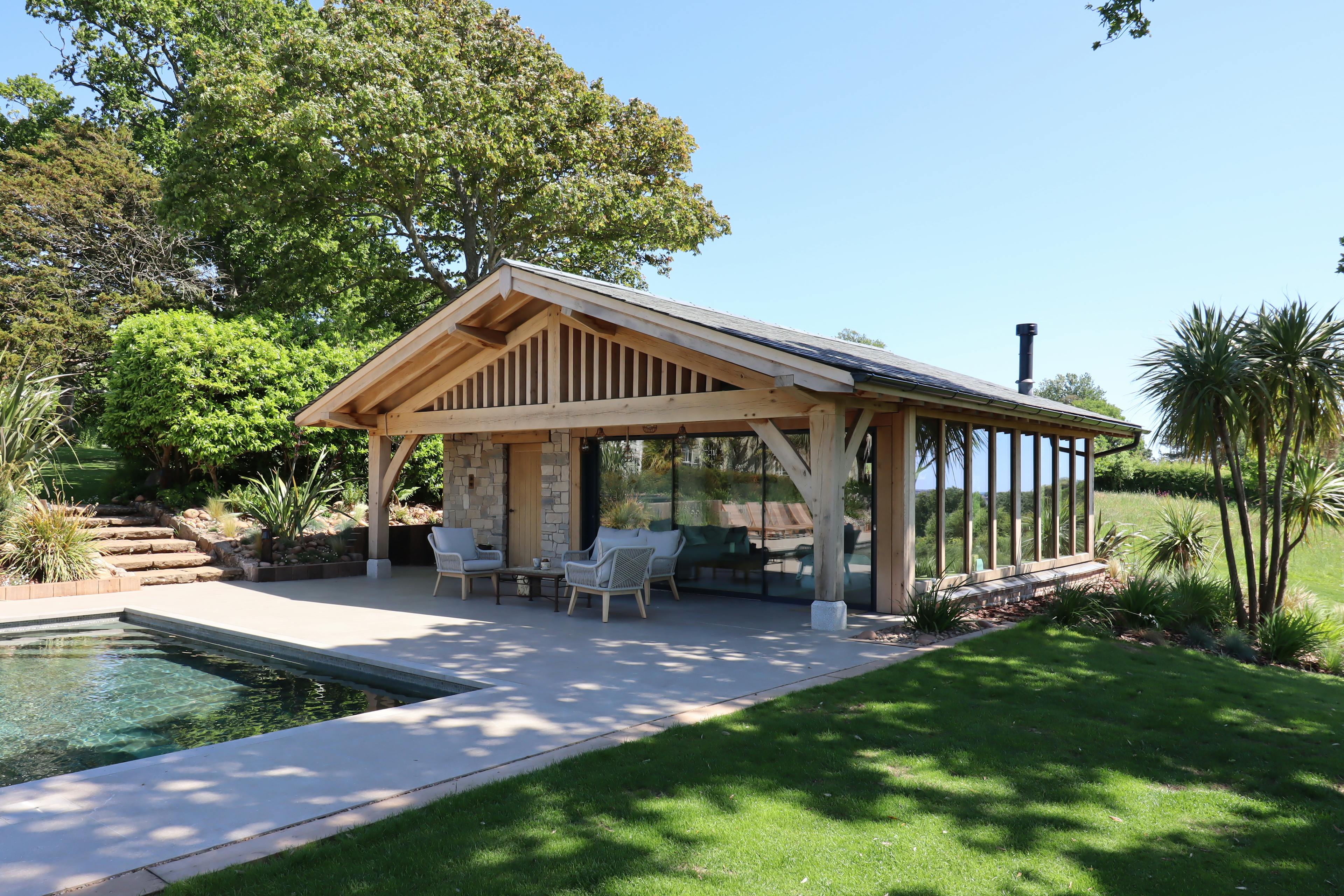 A swimming pool and an oak framed pool building annexe with low pitch roof and brise soleil, patio and outdoor seating, set in a large garden