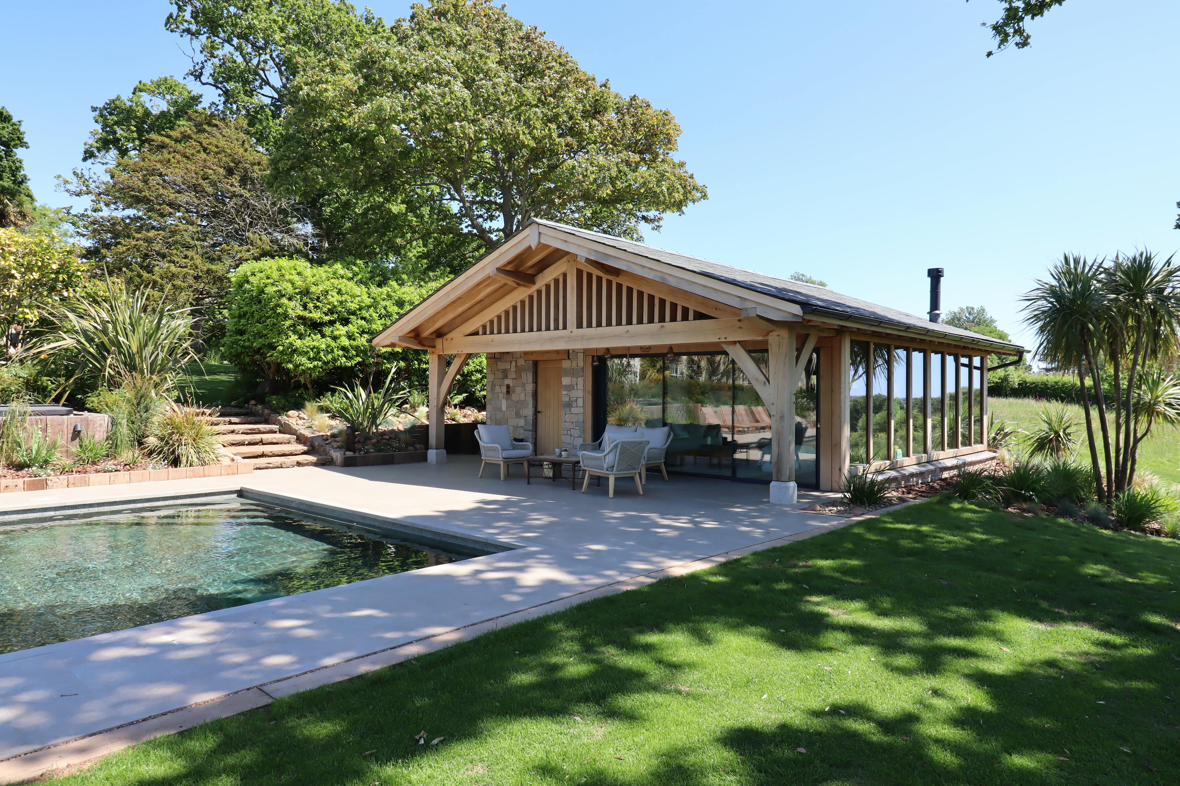 A swimming pool and an oak framed pool building annexe with low pitch roof and brise soleil, patio and outdoor seating, set in a large garden