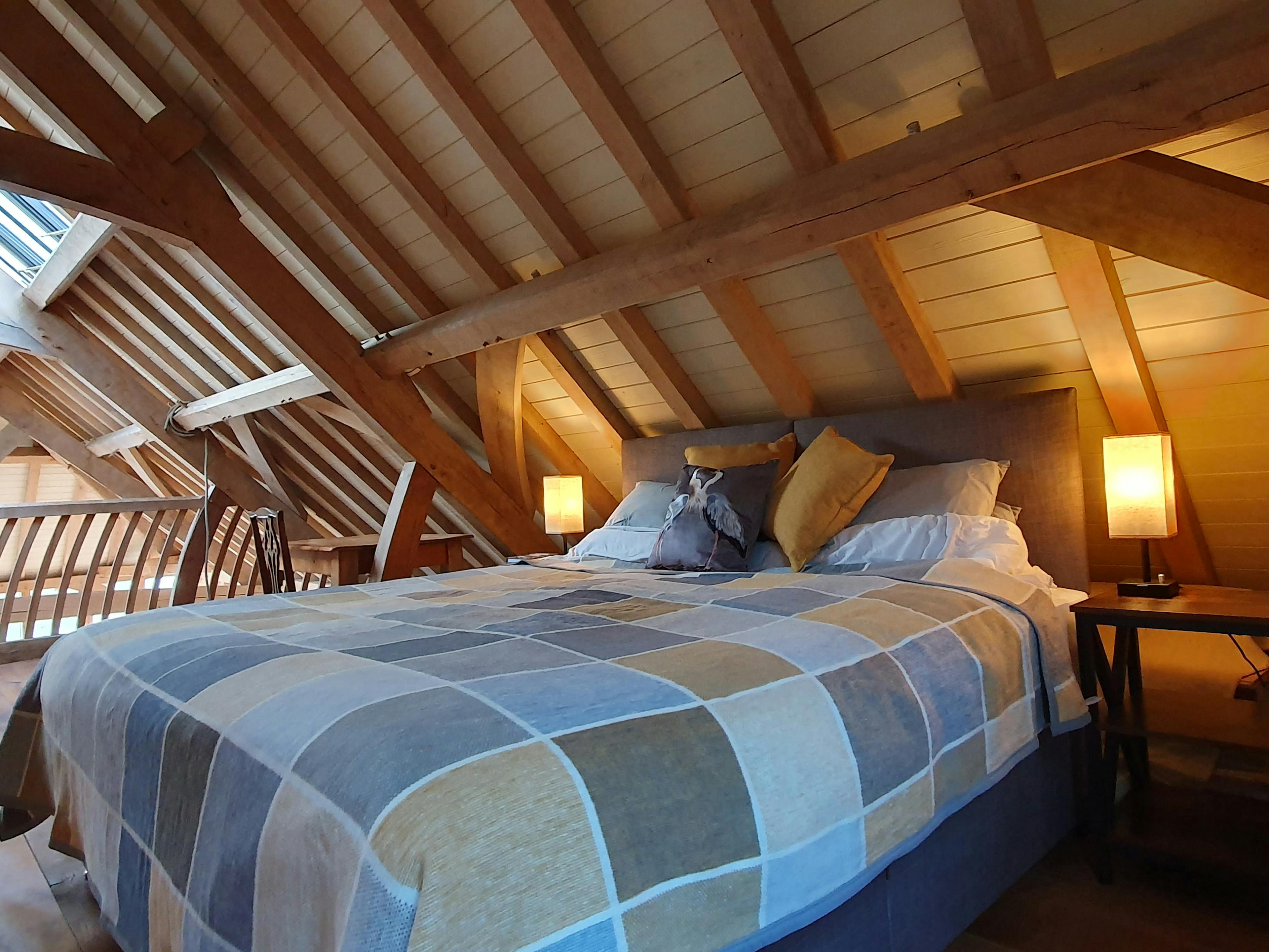 A double bed on a mezzanine area in an oak framed boathouse