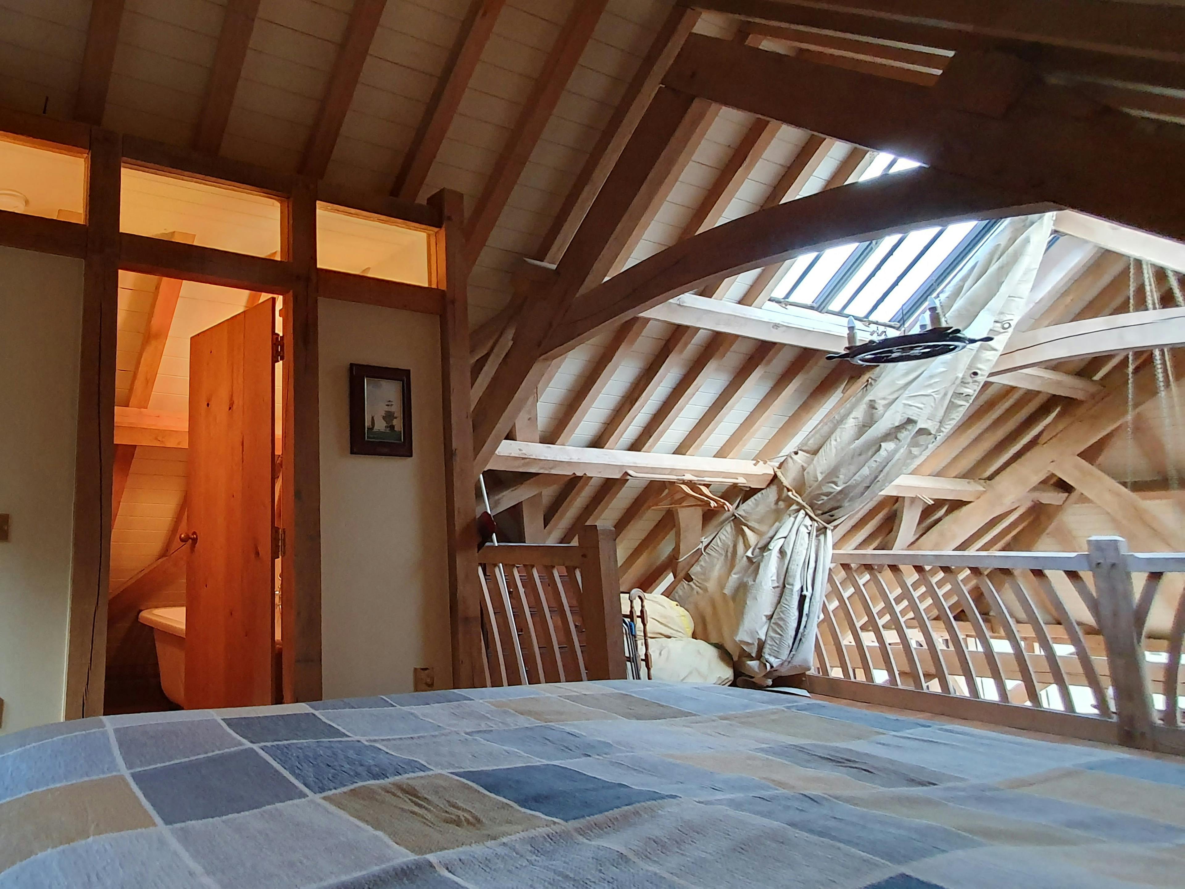 A double bed with an ensuite bathroom on a mezzanine area in an oak framed boathouse