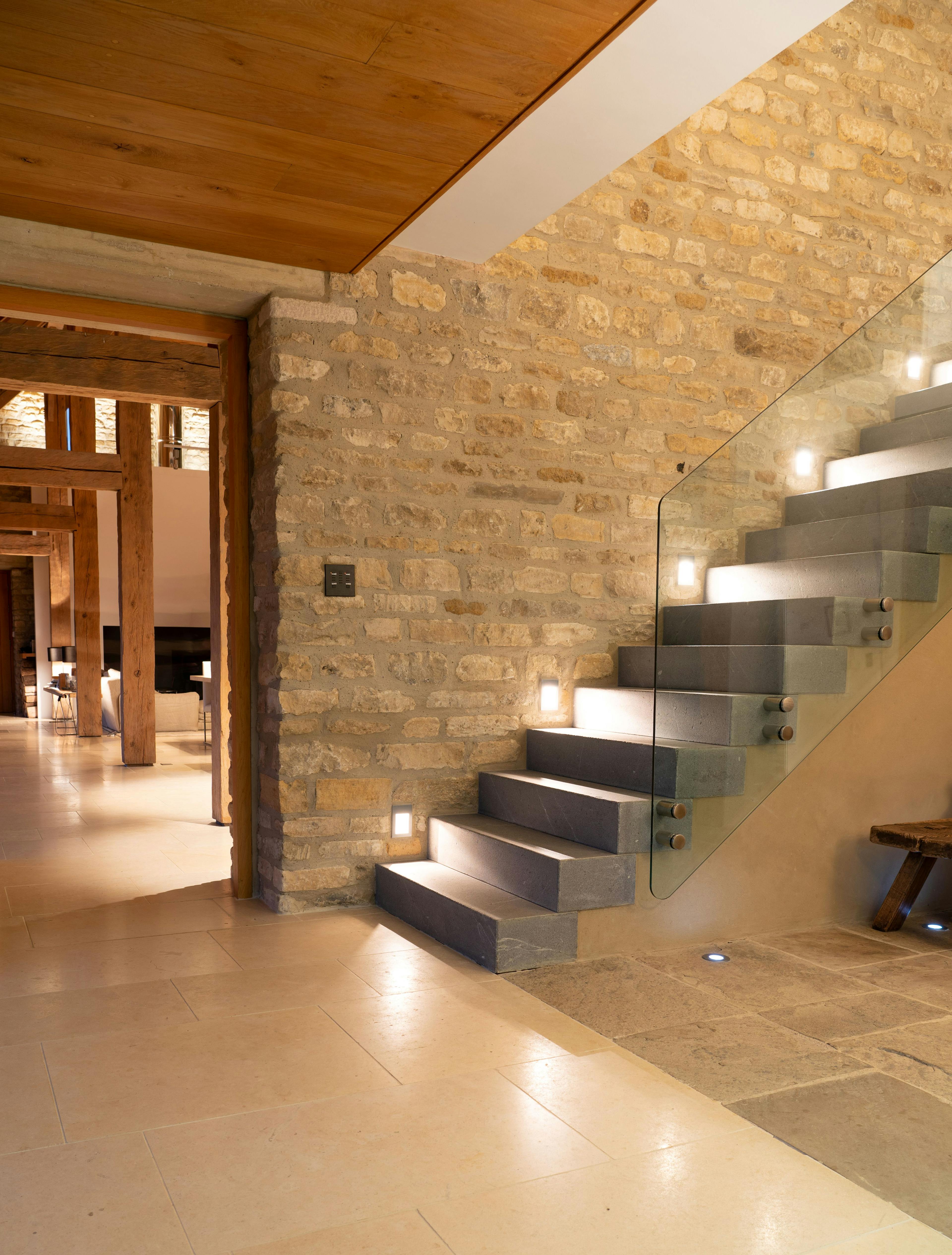 A night time image of a hallway and stairs of a spacious renovated oak-framed barn featuring exposed rustic beams, and a contemporary finish