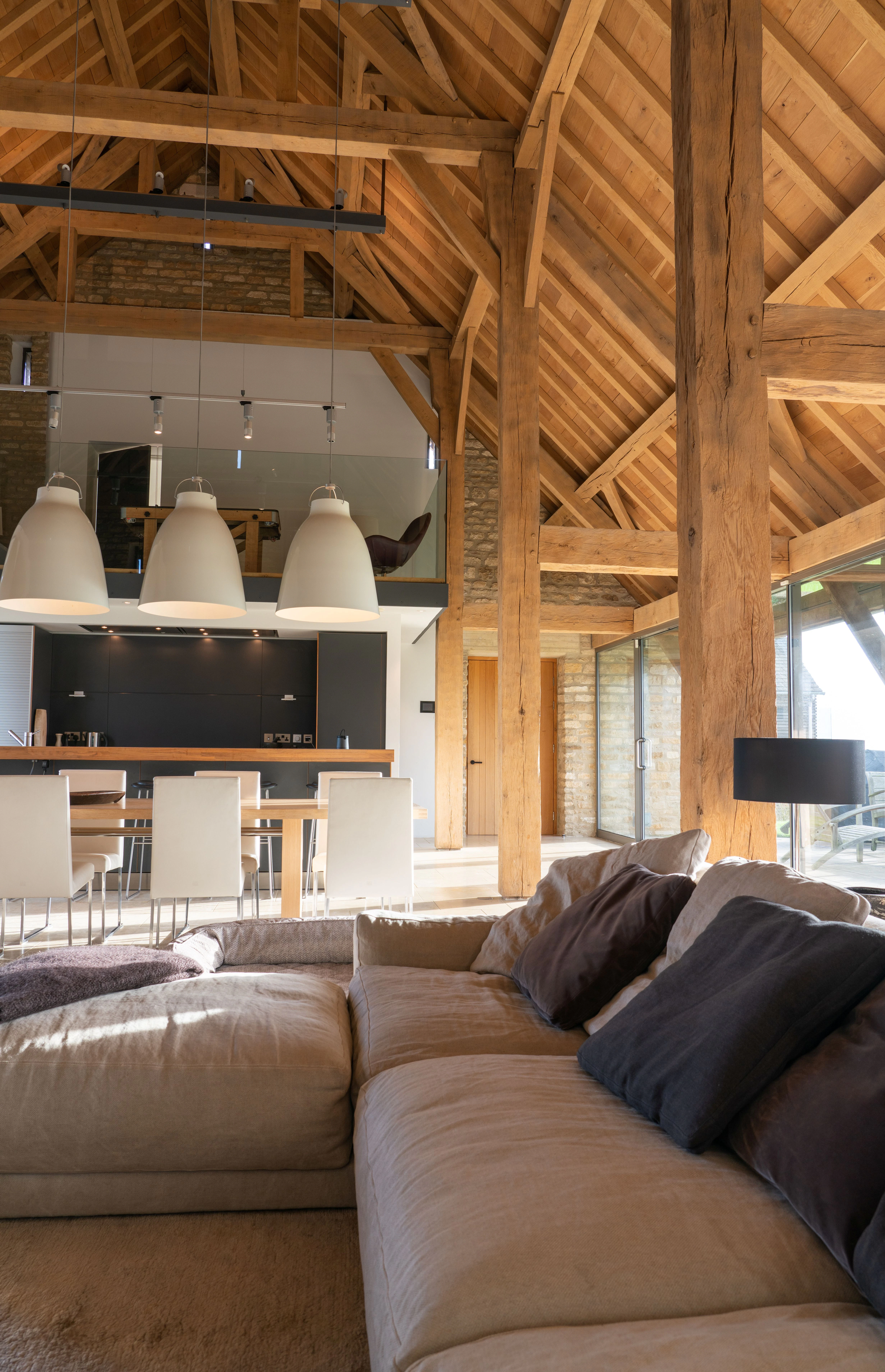 Interior of a spacious renovated oak-framed barn featuring a vaulted ceiling, exposed rustic beams, and a contemporary open-plan living, kitchen and dining area