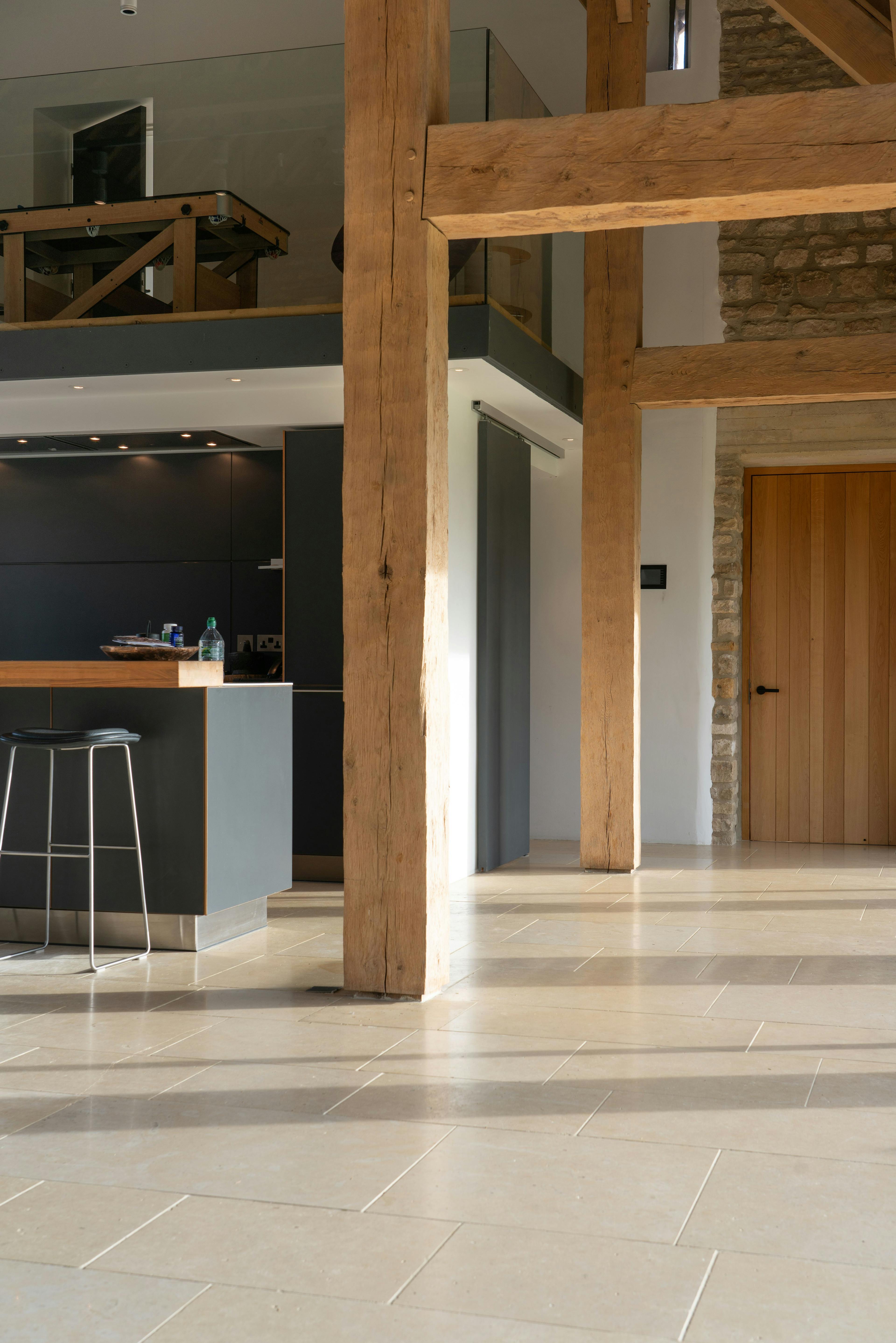 Sunlight beams onto an interior of a spacious renovated oak-framed barn featuring a vaulted ceiling, exposed rustic beams, and a contemporary open-plan living area