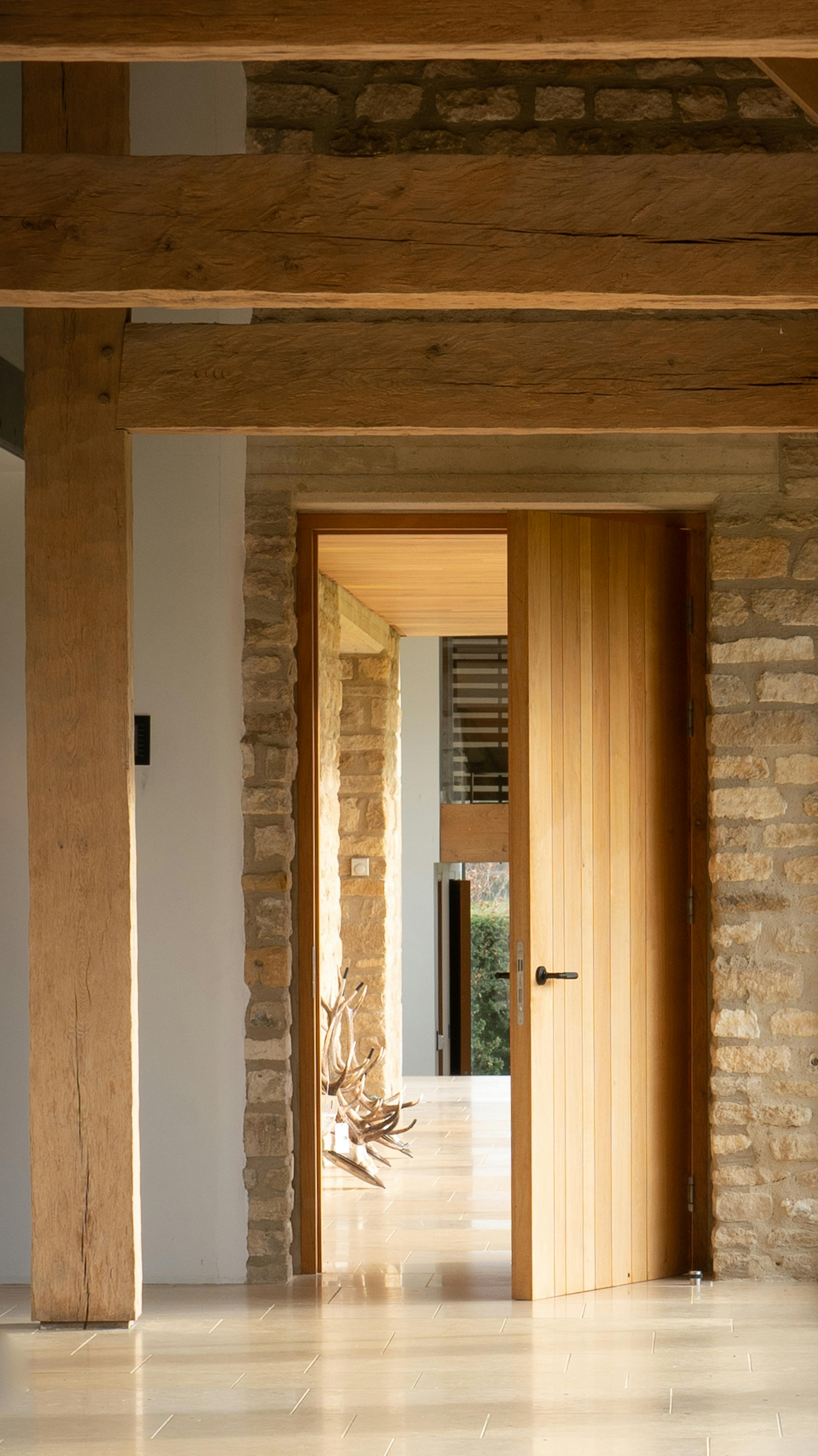 An open door of a spacious renovated oak-framed barn featuring exposed rustic beams, and a contemporary interior finish