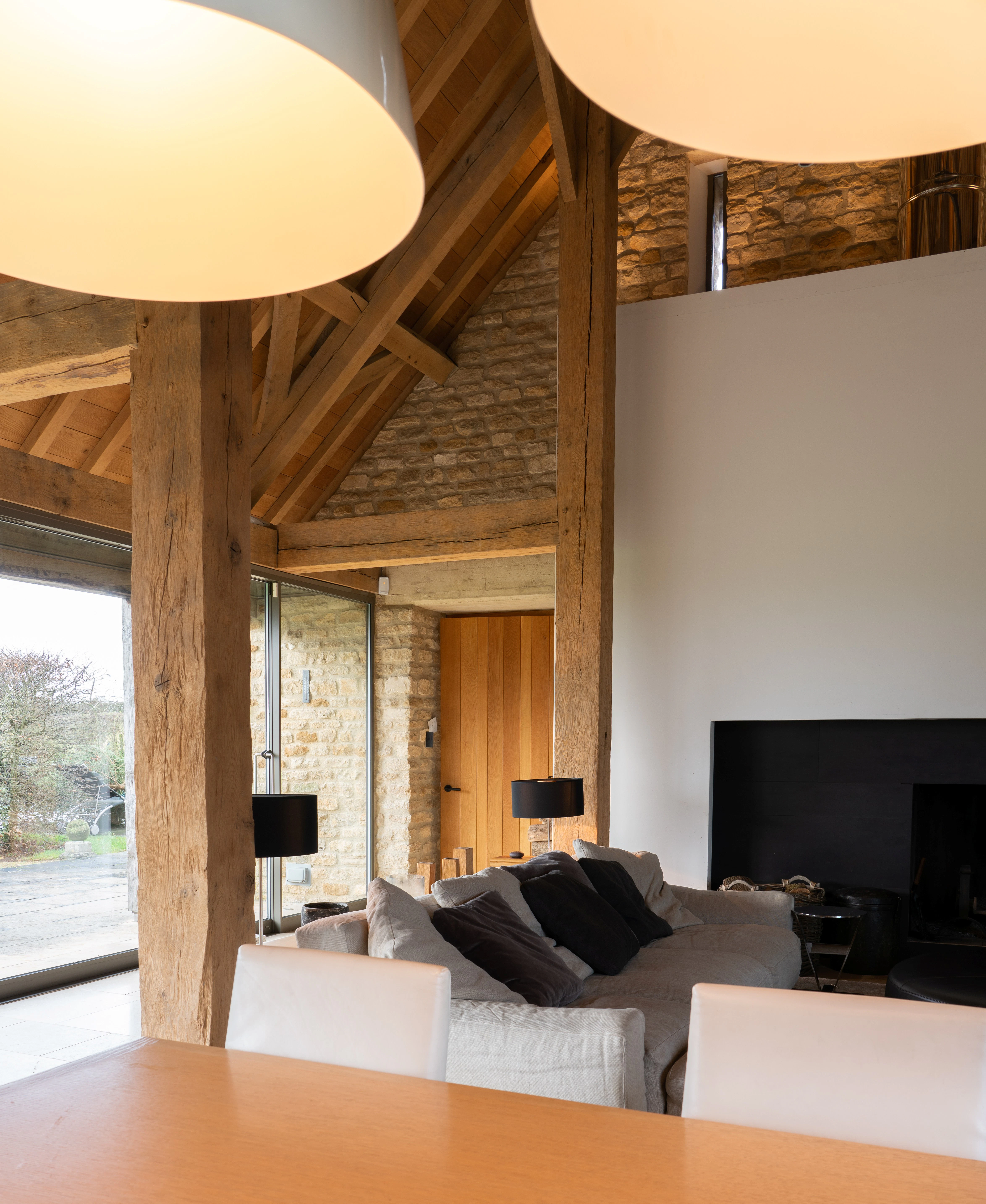 Interior of a spacious renovated oak-framed barn featuring a vaulted ceiling, exposed rustic beams, and a contemporary open-plan dining and lounge area