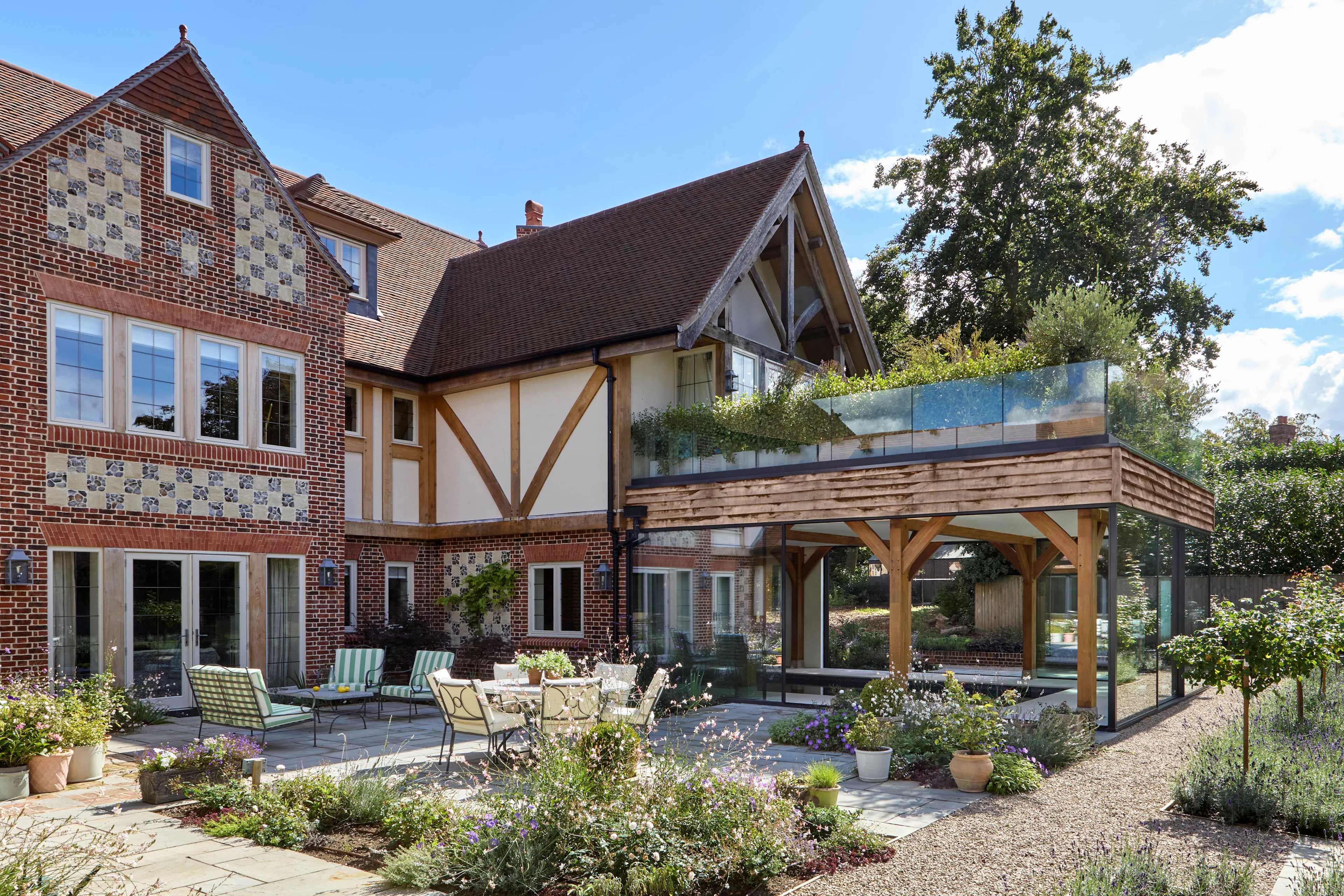 The rear of a large 6 bedroom oak framed home with a glazed swimming pool room terrace with outdoor seating