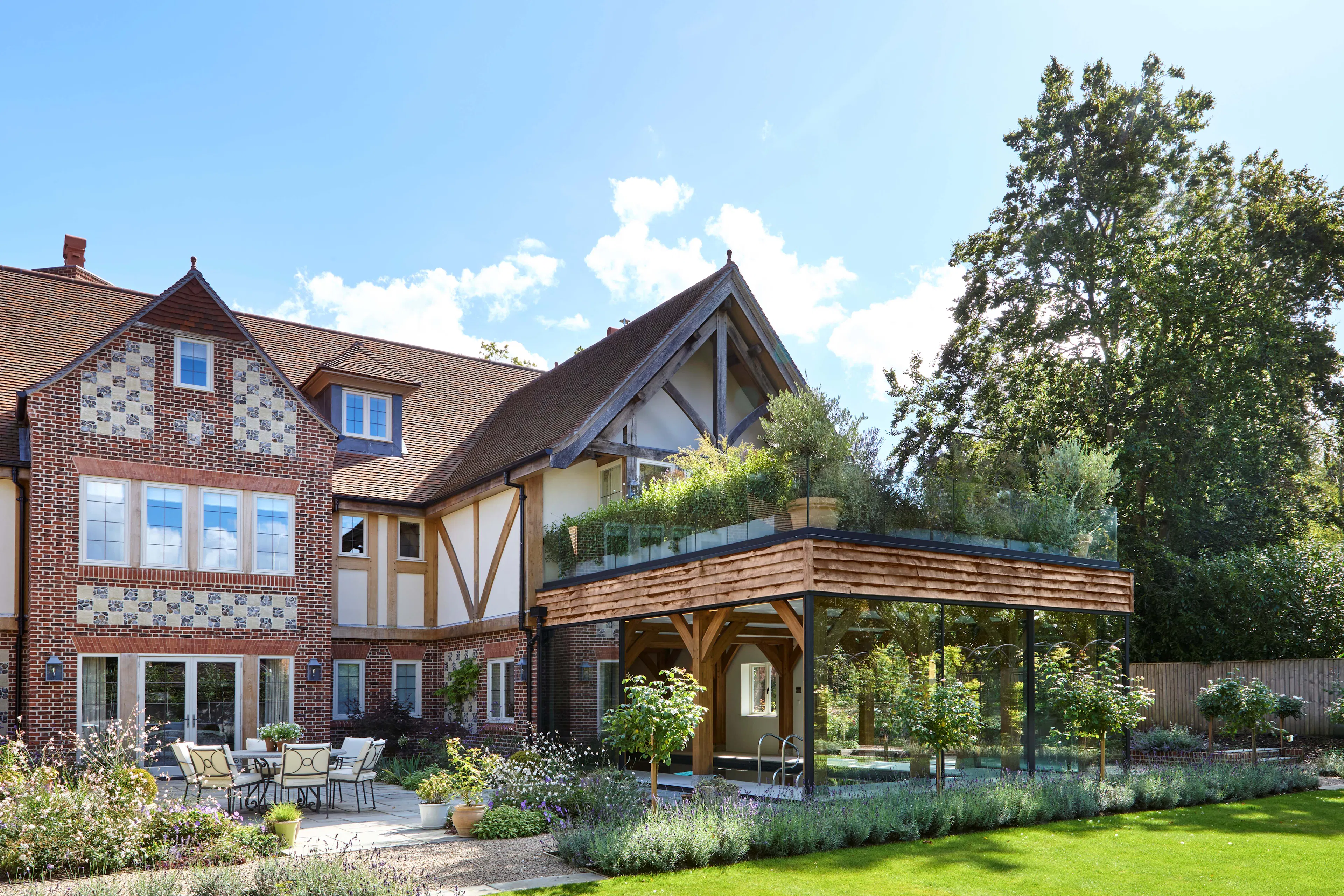 The rear of a large 6 bedroom oak framed home with a glazed swimming pool room and green lawn