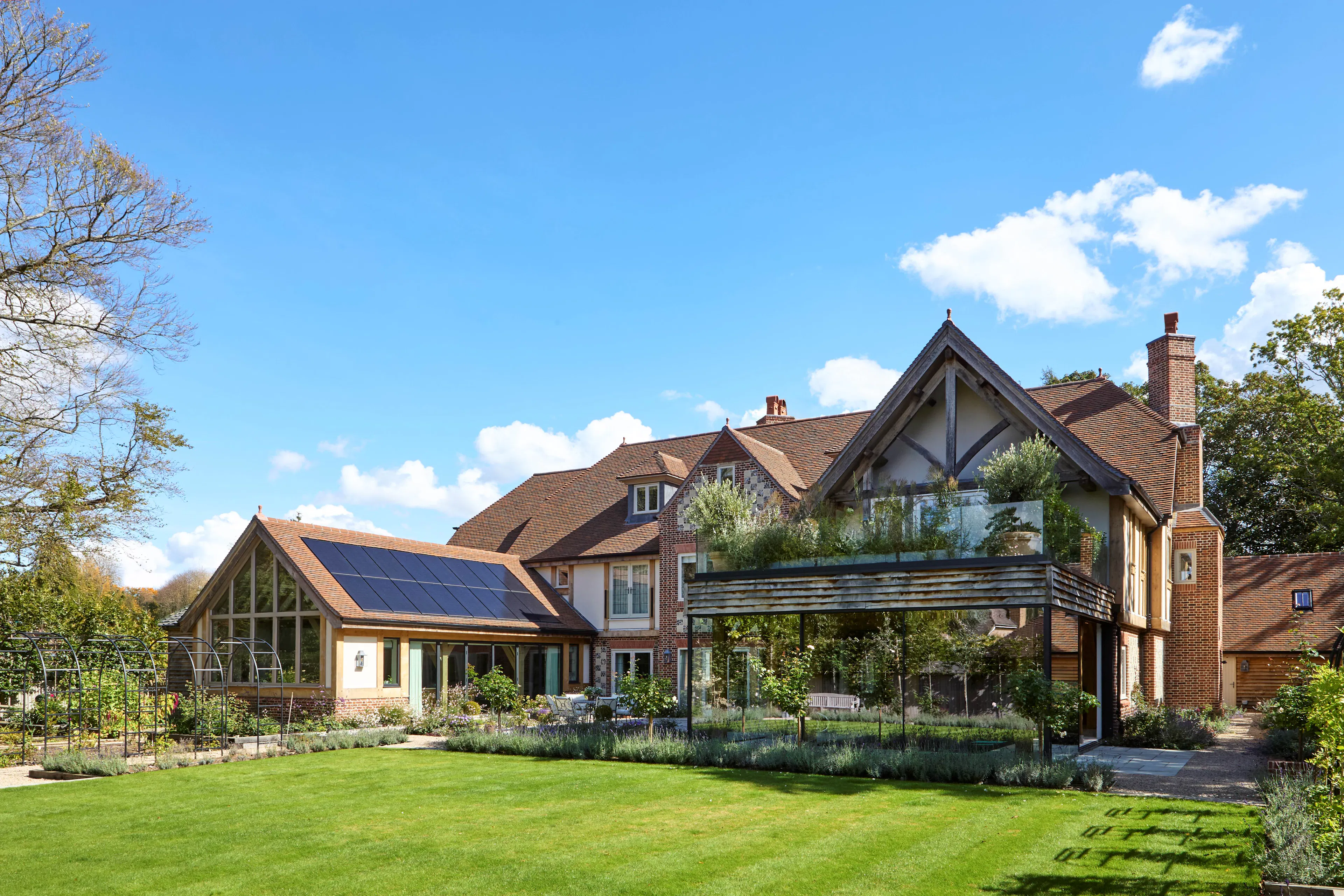 The rear of a large 6 bedroom oak framed home with a glazed swimming pool room and large green lawn