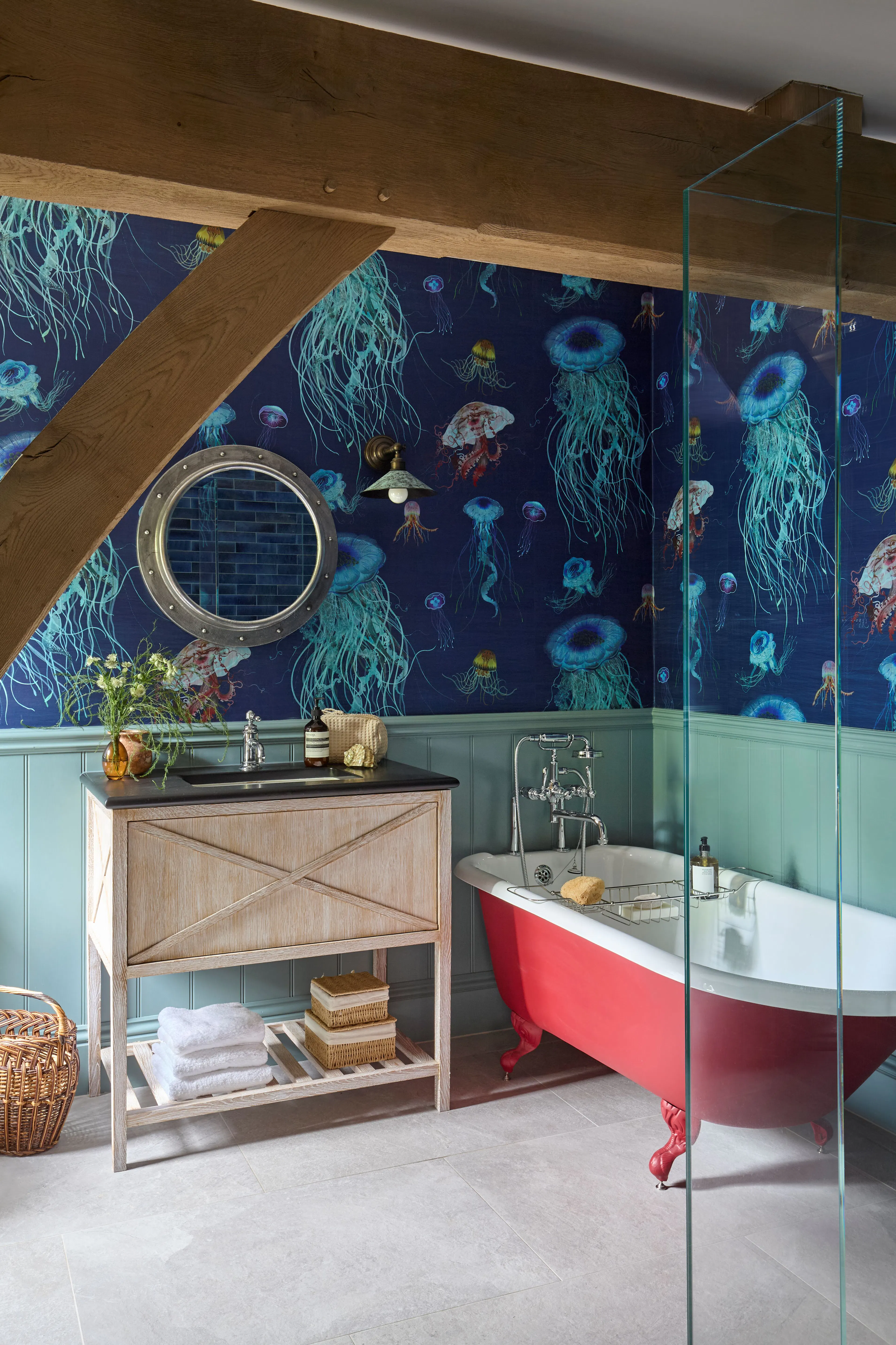 A bathroom with bright blue jellyfish wall paper and a red freestanding bath in a large 6 bedroom oak framed home