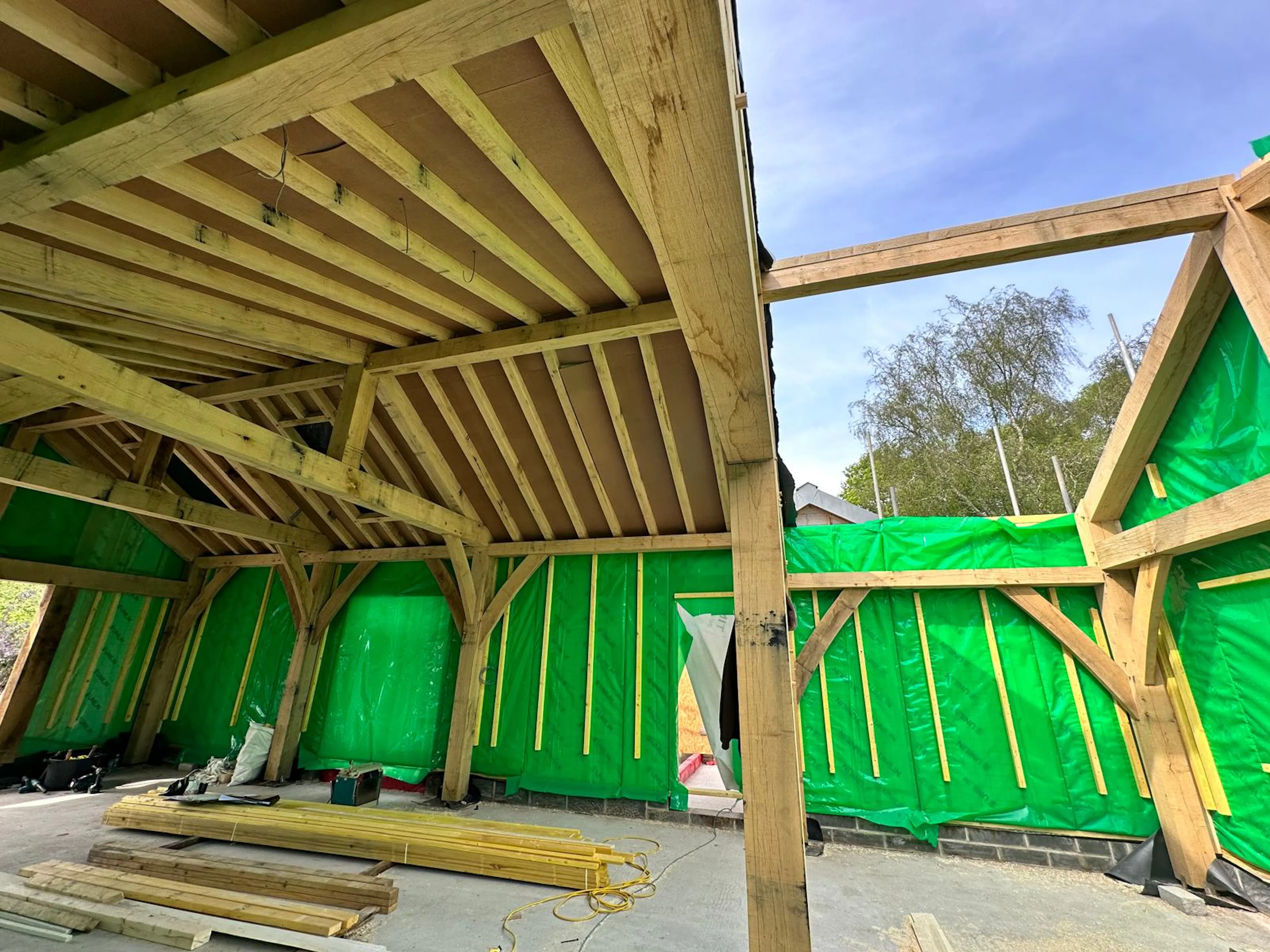 Two carpenters installing prefabricated panels into a structural oak timber frame at a building site