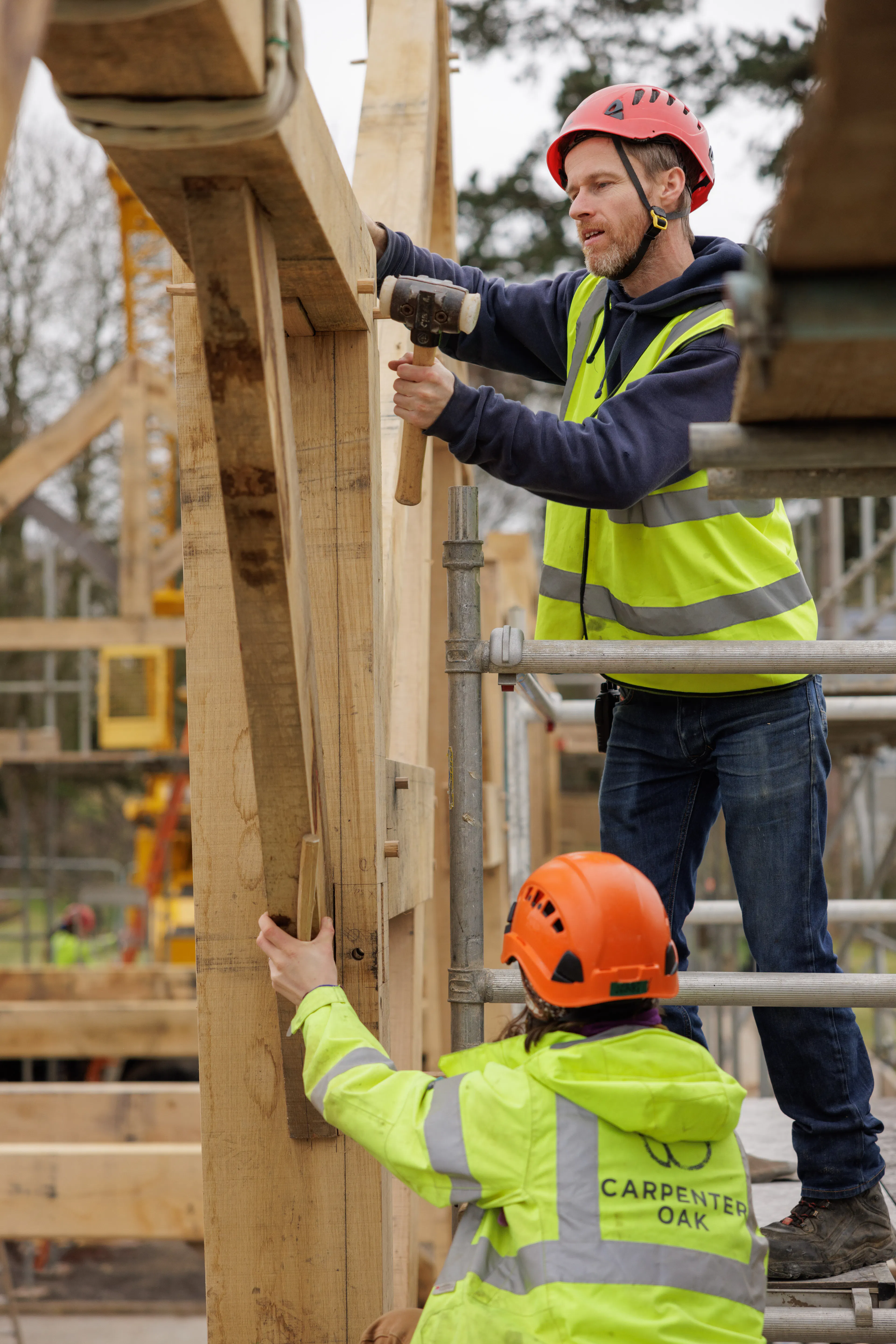 Two carpenters knocking in wooden pegs during installation of a large oak frame home