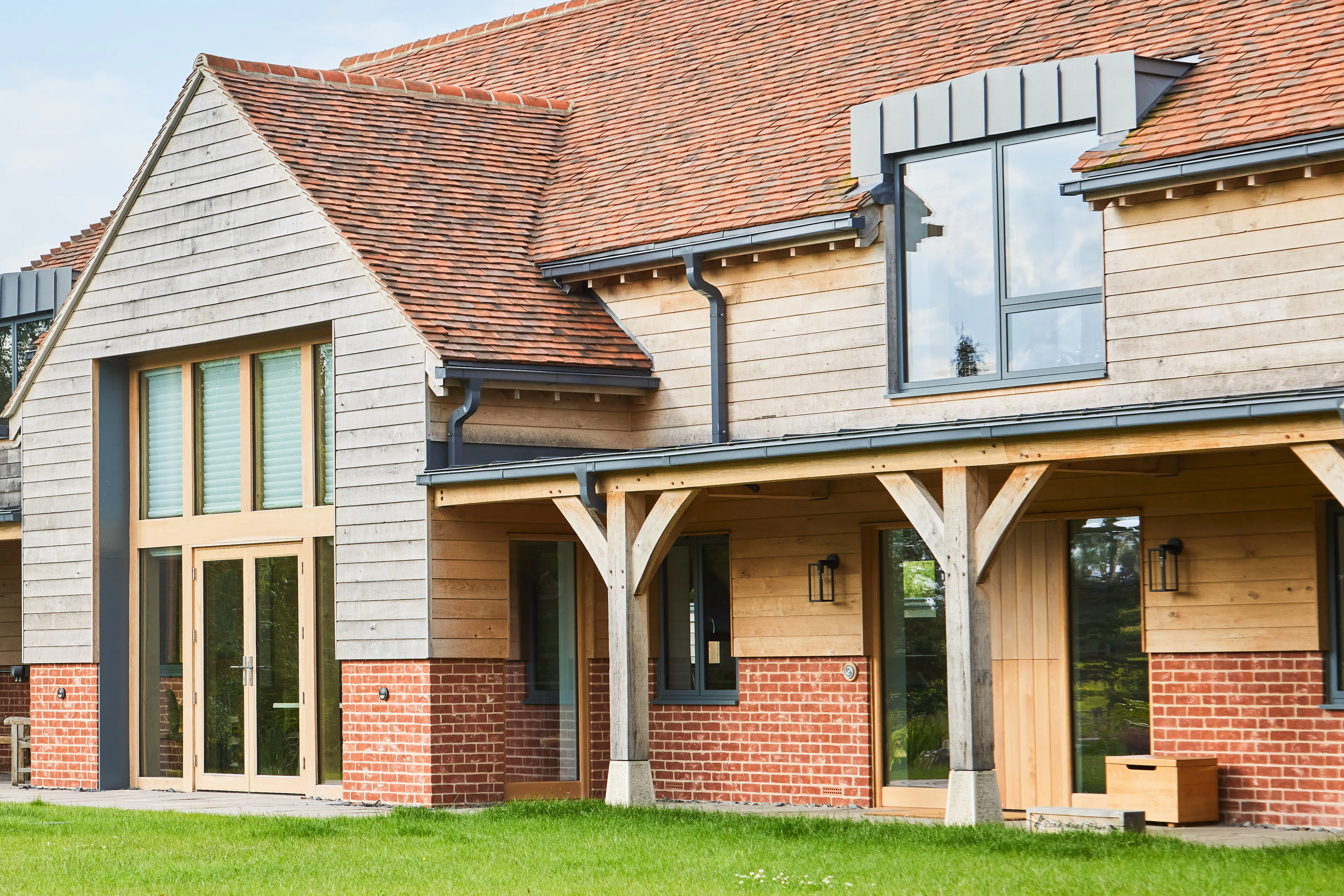 A green lawn in front of a large oak framed home with an oak framed veranda