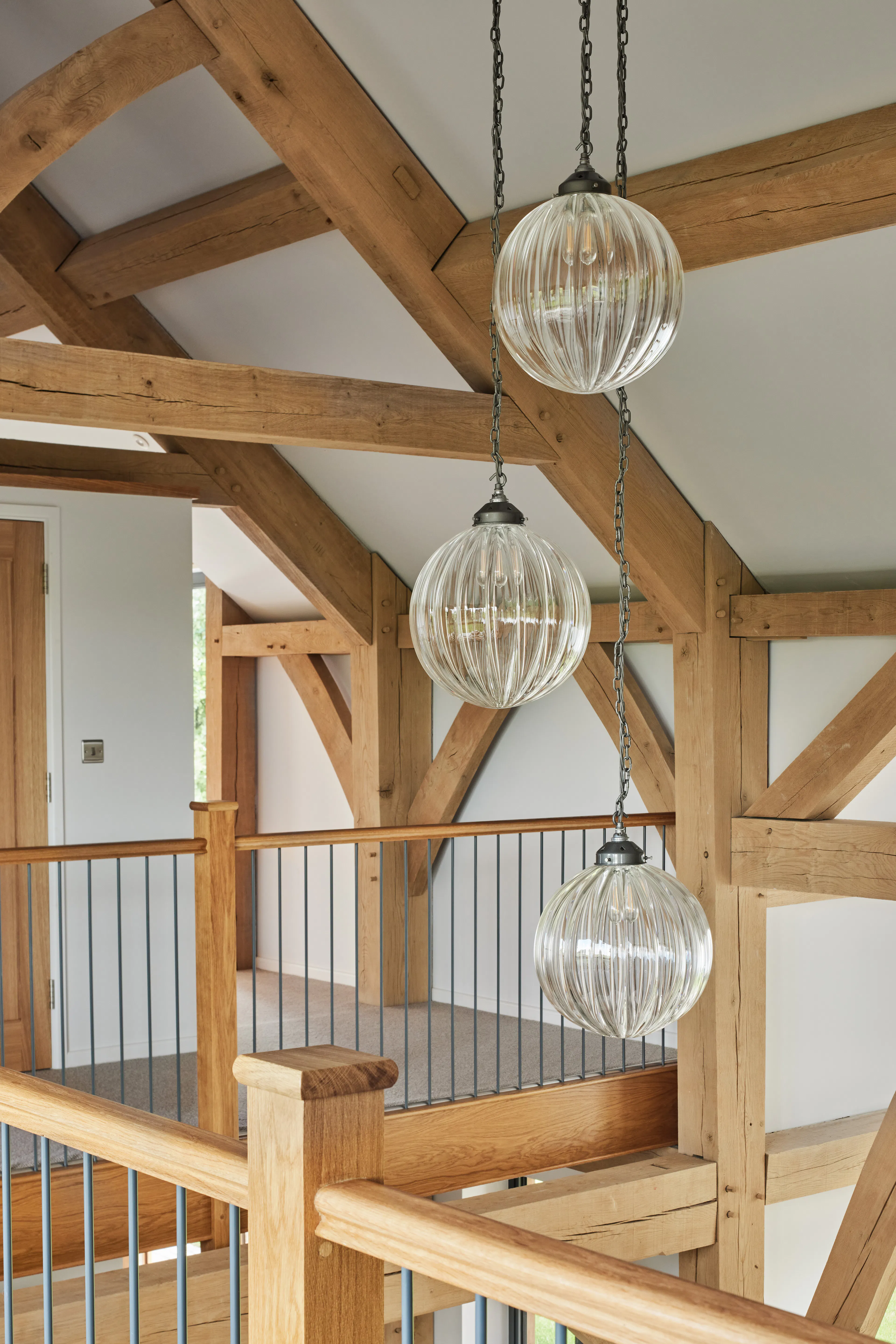 A mezzanine landing area and white cylindrical lights hanging from the ceiling in a large oak framed home