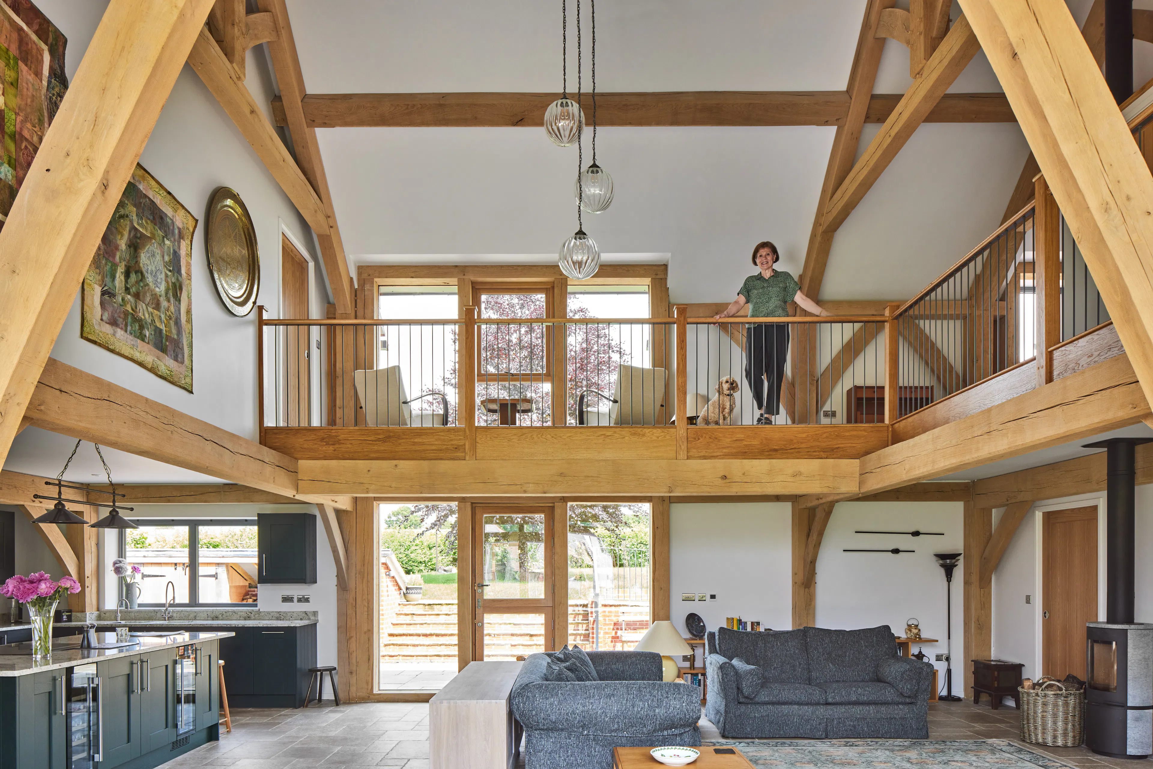 The homeowner and her dog on a mezzanine landing area in a large oak framed home with an open plan living, dining and kitchen space with vaulted ceilings