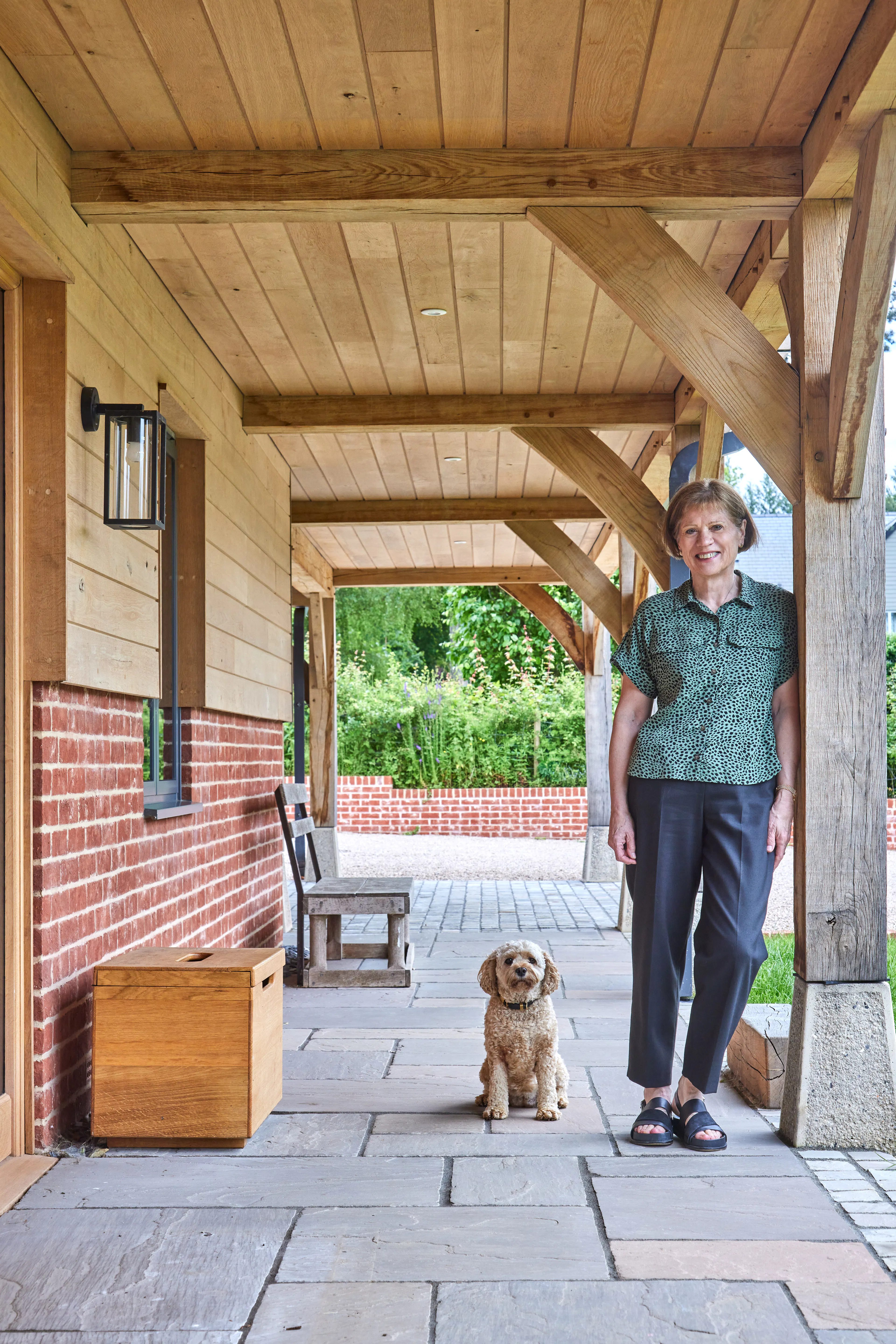 An oak frame veranda outside a large oak frame home with the home's owner and her small white dog