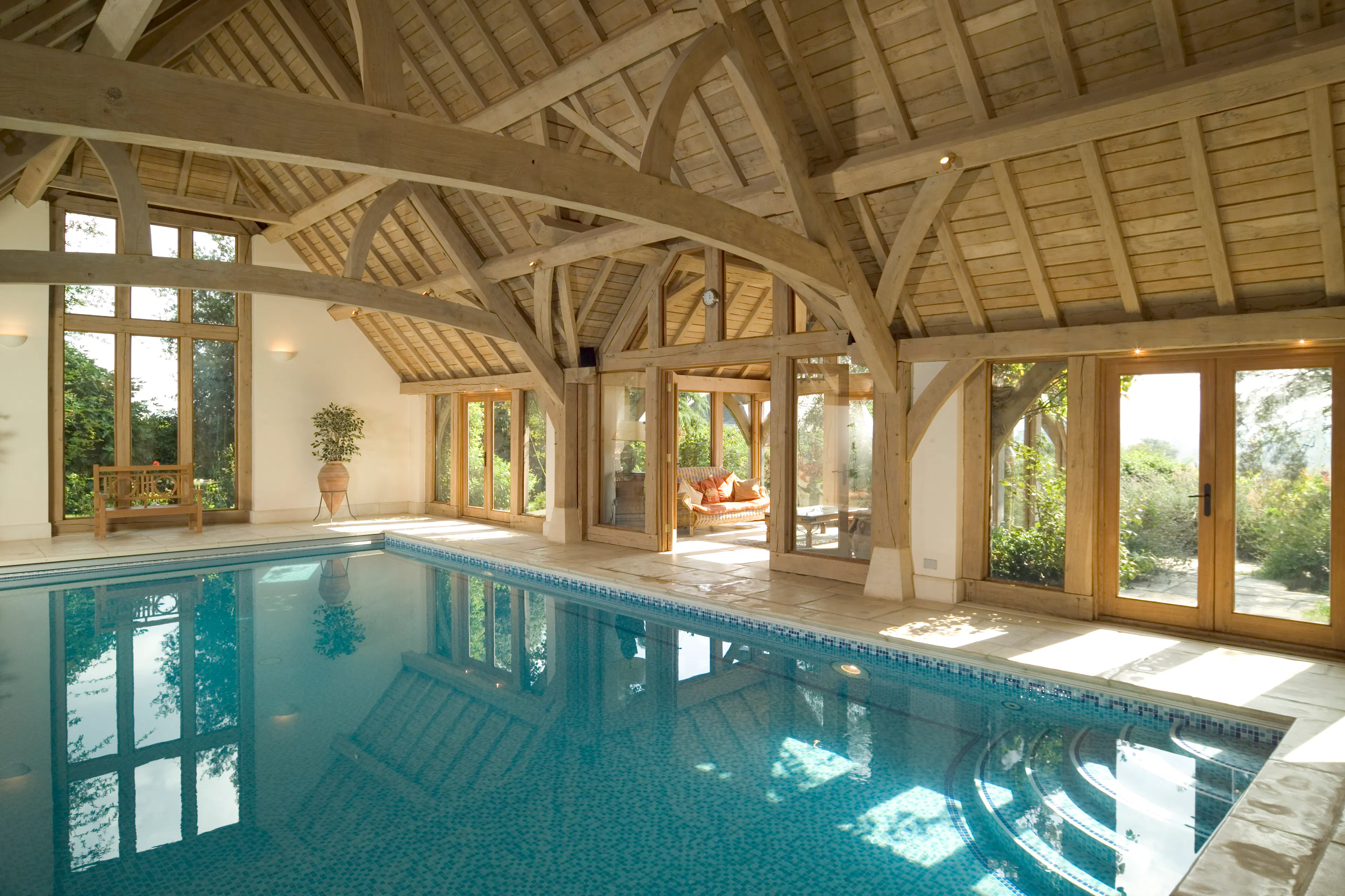 An oak framed swimming pool with sun coming through glazed windows