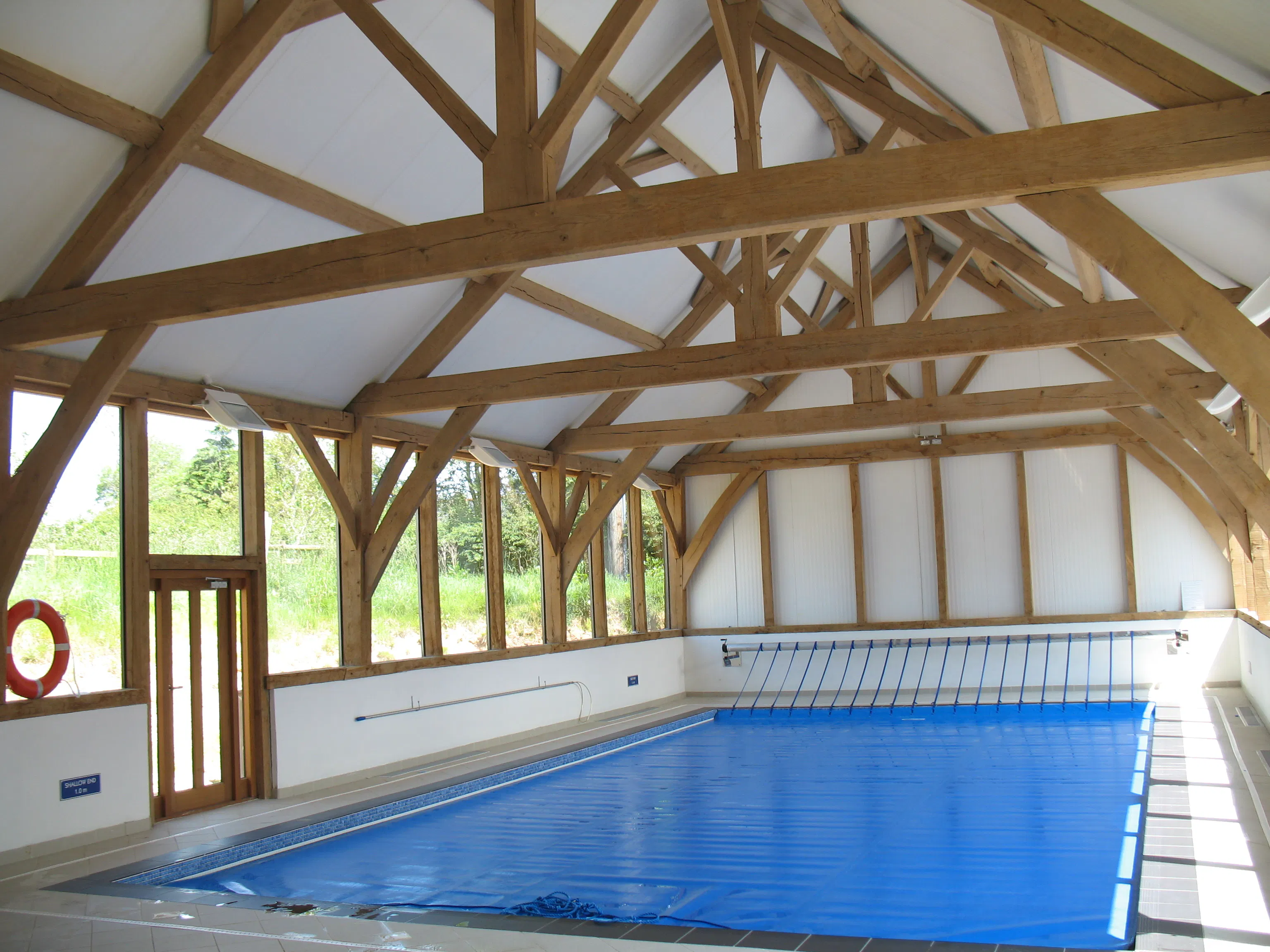 An oak framed swimming pool with sun coming through glazed windows