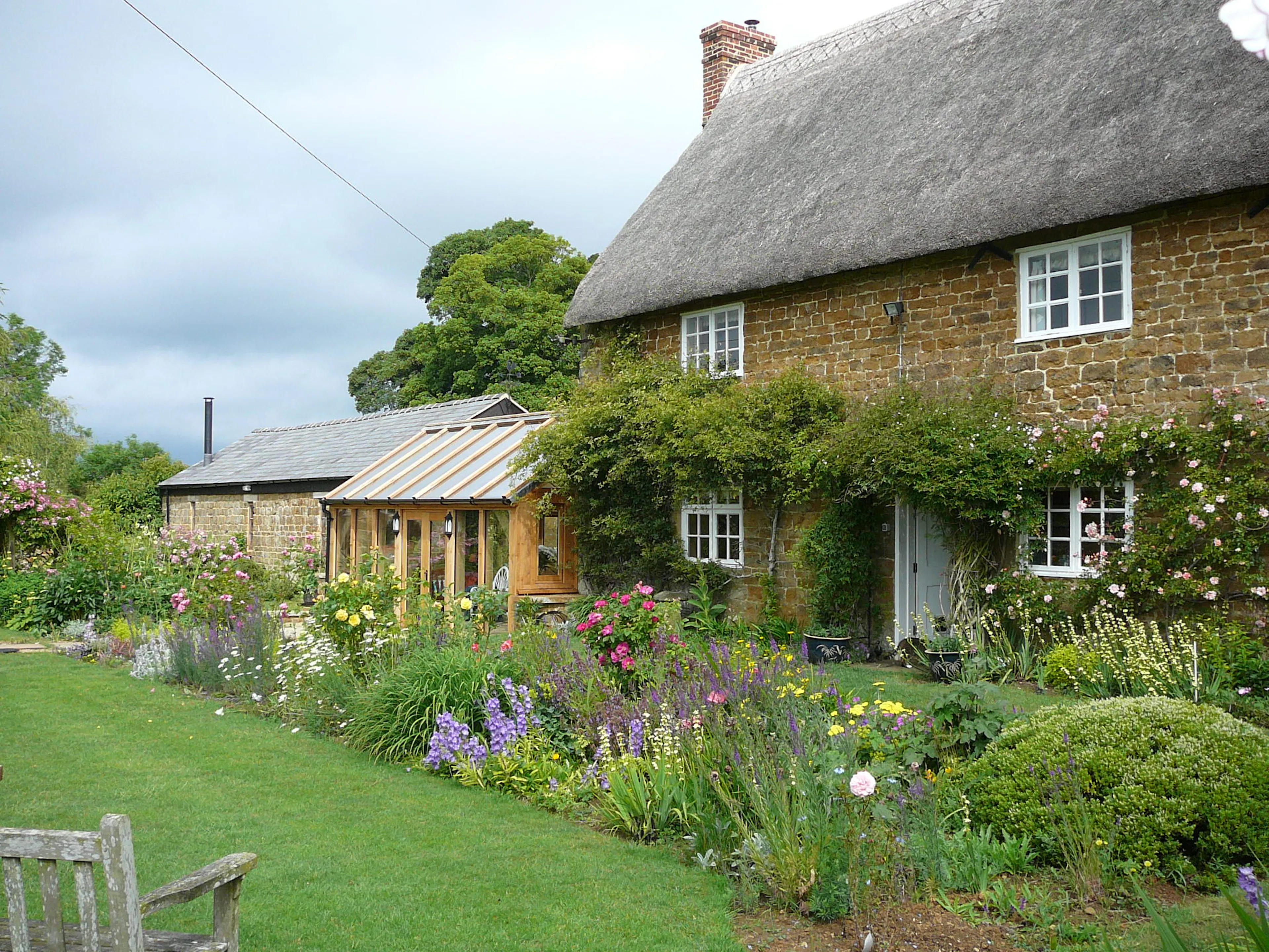 A link extension sunroom to a thatched cottage with a pretty flowering garden