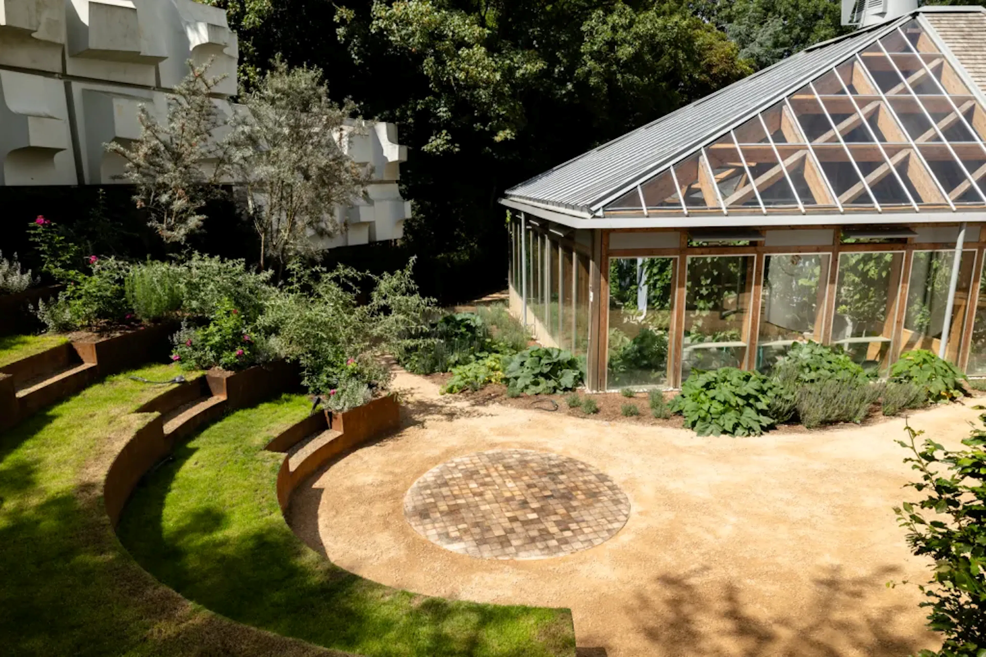 A larch glulam frame of a pyramidic greenhouse building next to a green terraced amphitheatre