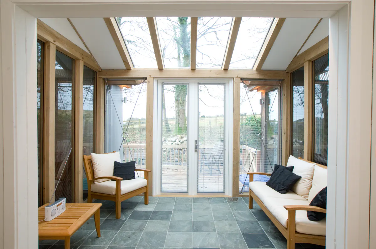 An oak framed sun room or garden room extension with glazed rooflights, windows and French doors, and furnished with stylish wooden sofas & armchair