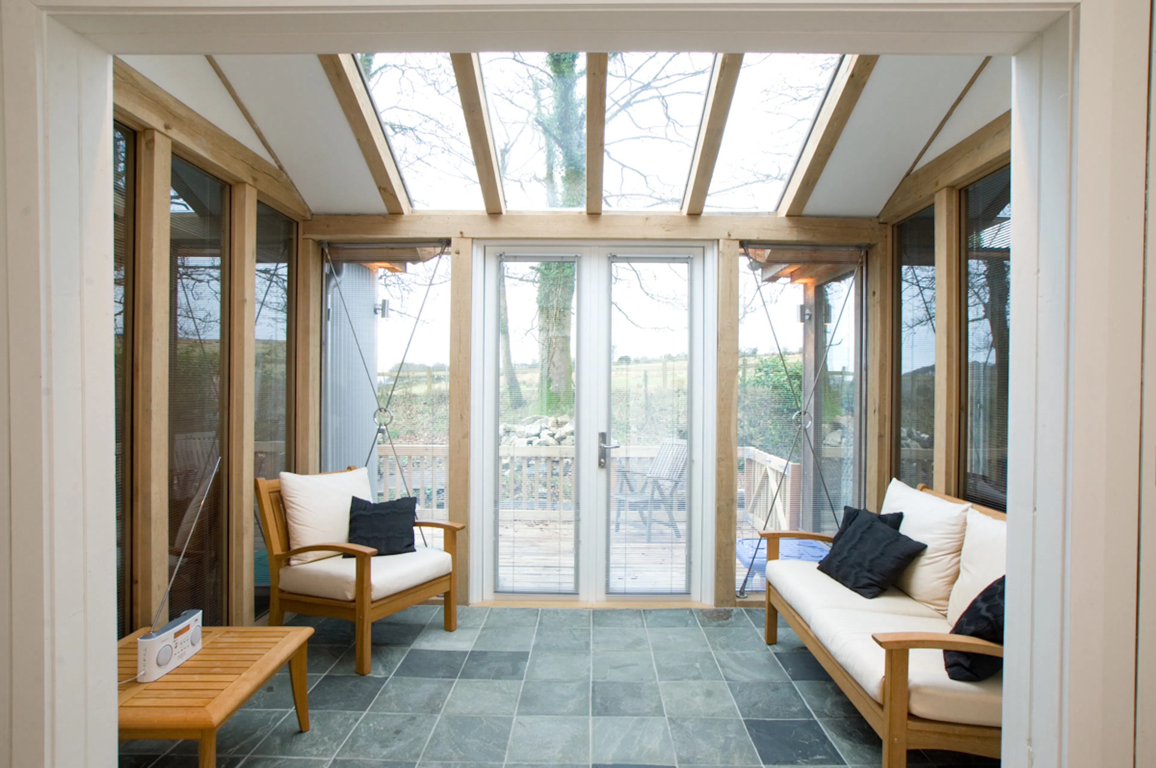 An oak framed sun room or garden room extension with glazed rooflights, windows and French doors, and furnished with stylish wooden sofas & armchair